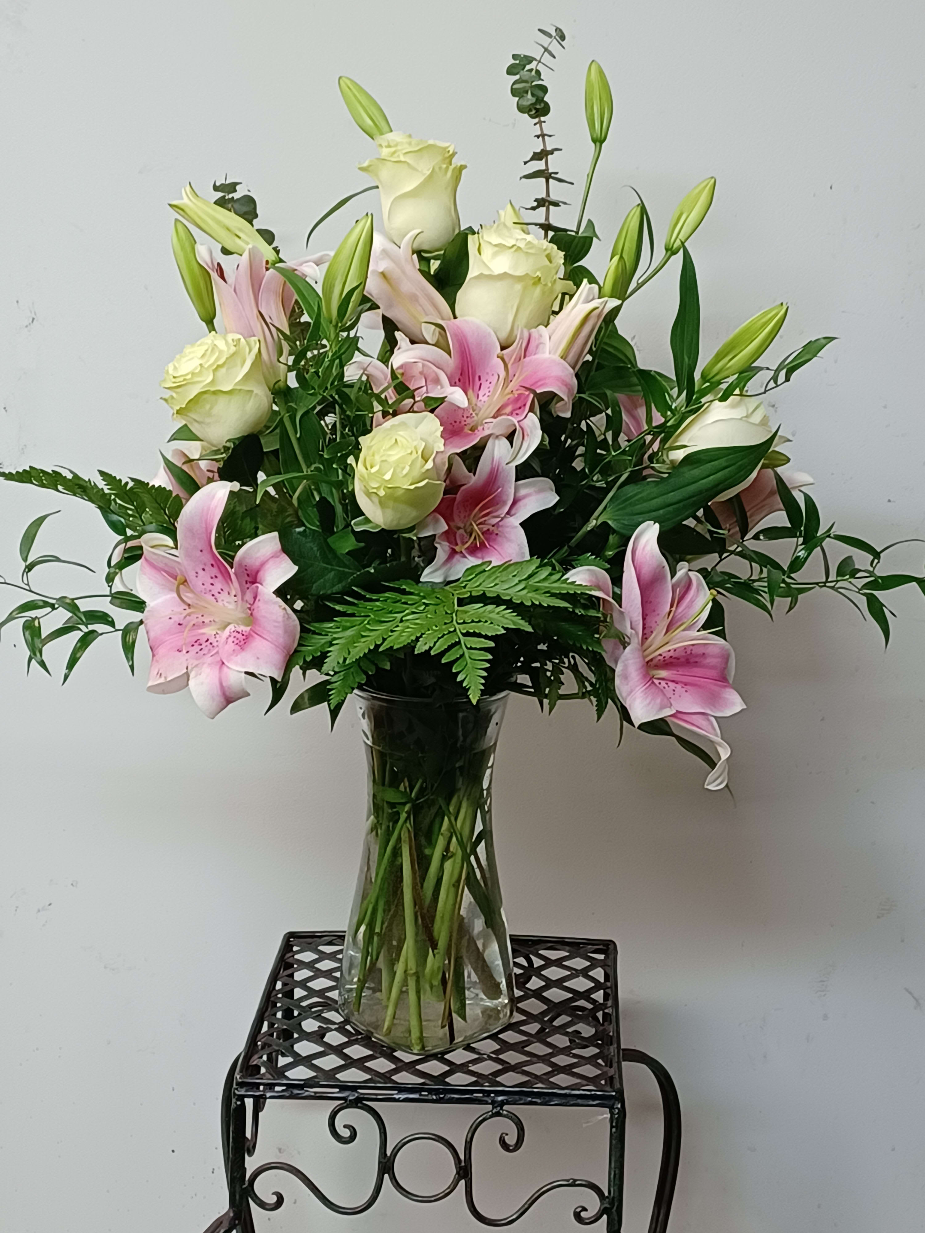 Pink lilies and white roses arranged in a clear glass vase