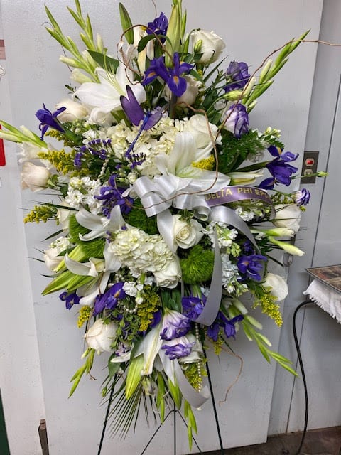 Large white and purple funeral spray on a stand with ribbon