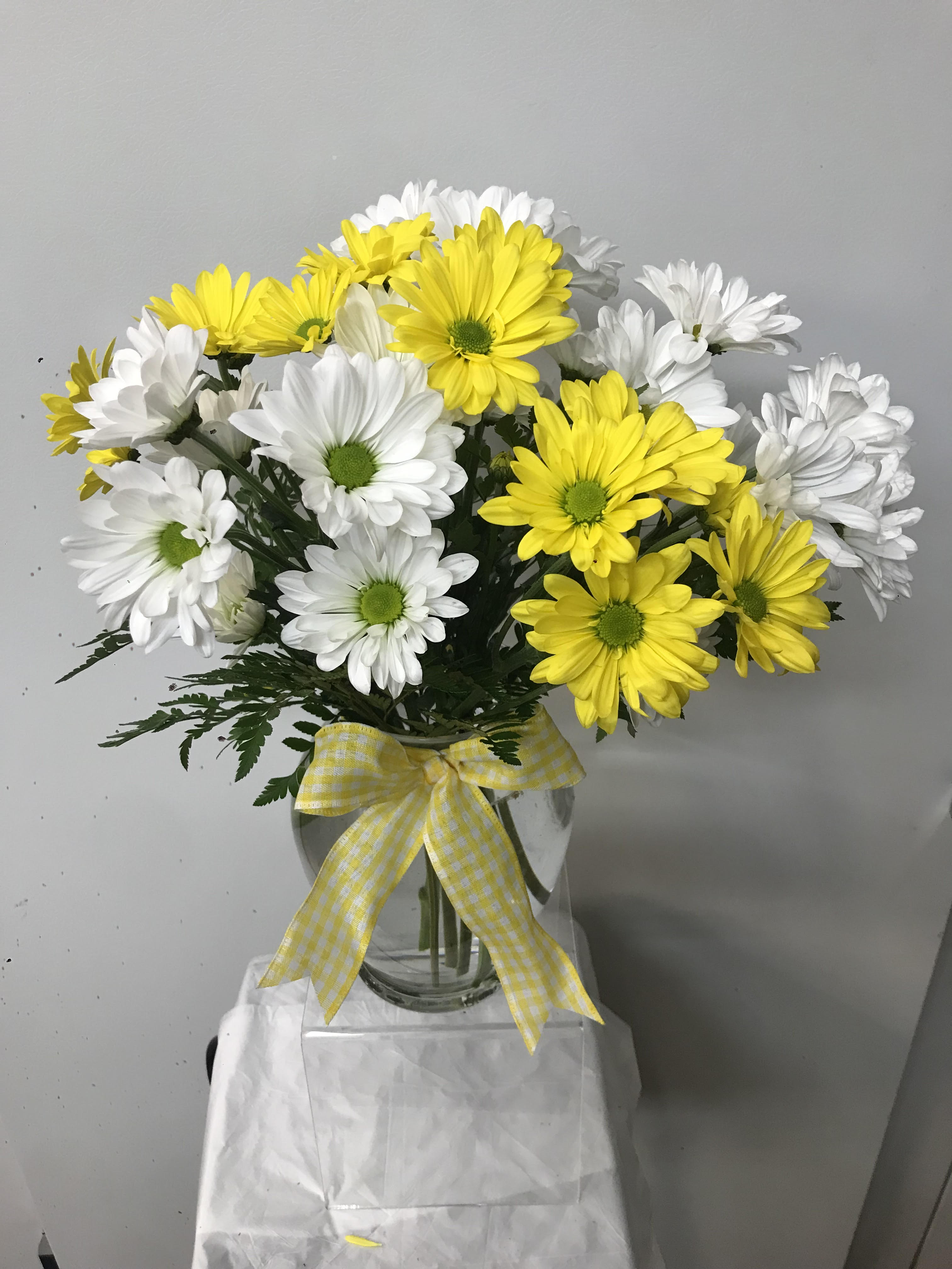Yellow and white daisy bouquet in a glass vase with a gingham ribbon