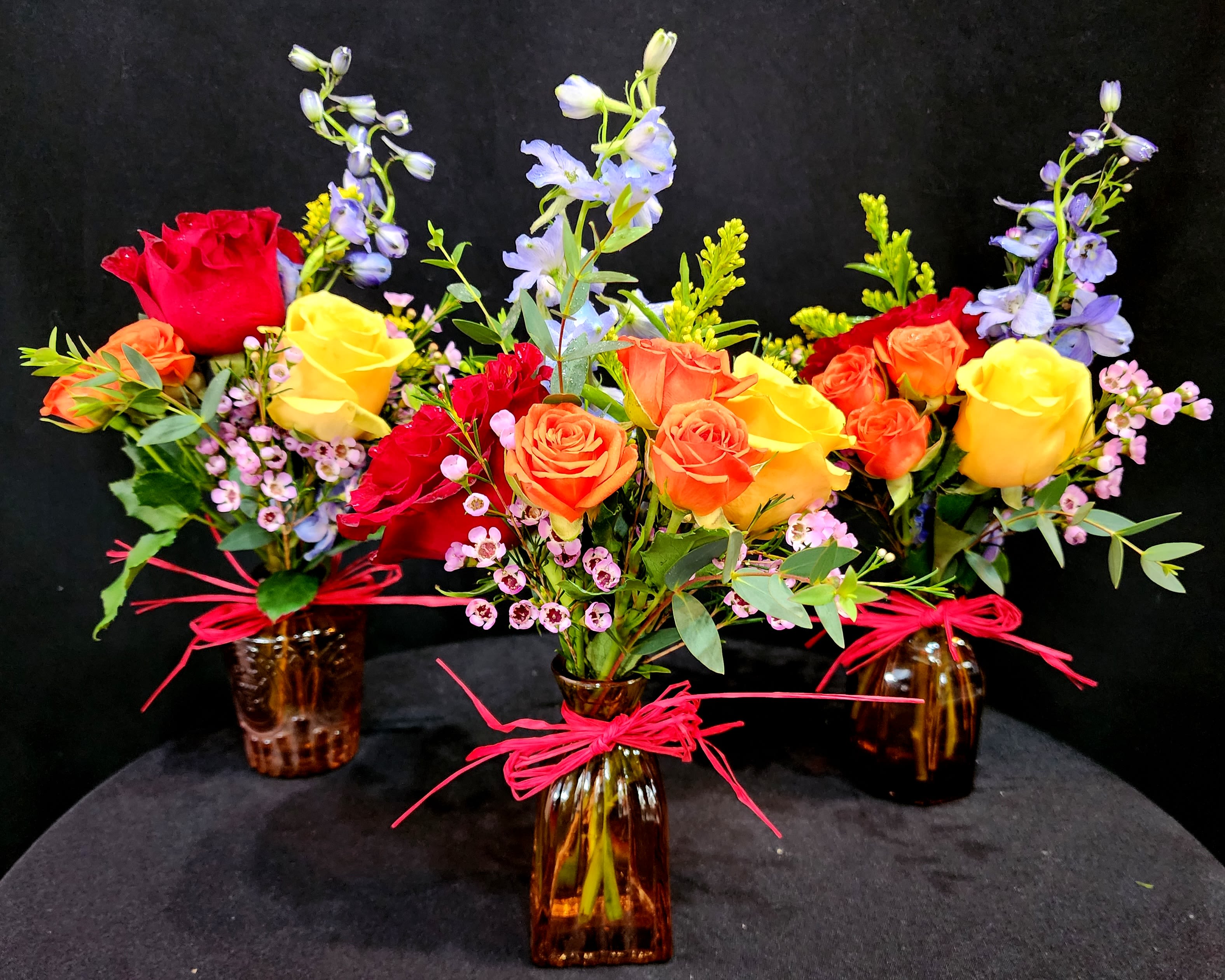 Three mixed rose bouquets in amber glass vases with pink ribbon ties
