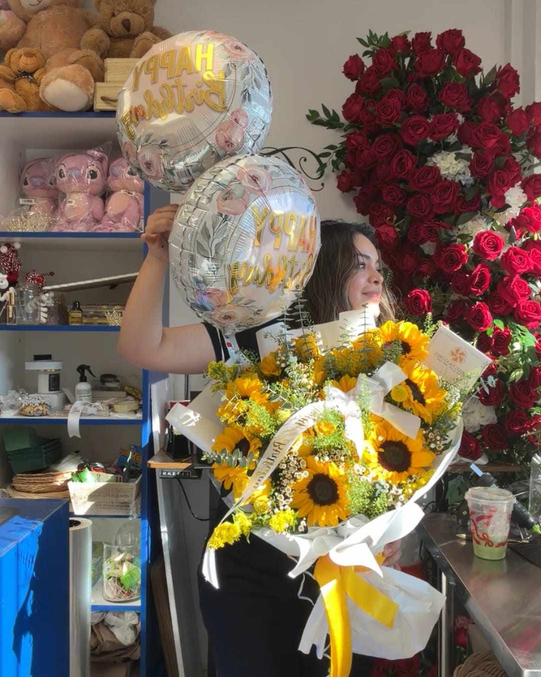 Woman holding a sunflower bouquet and two birthday balloons