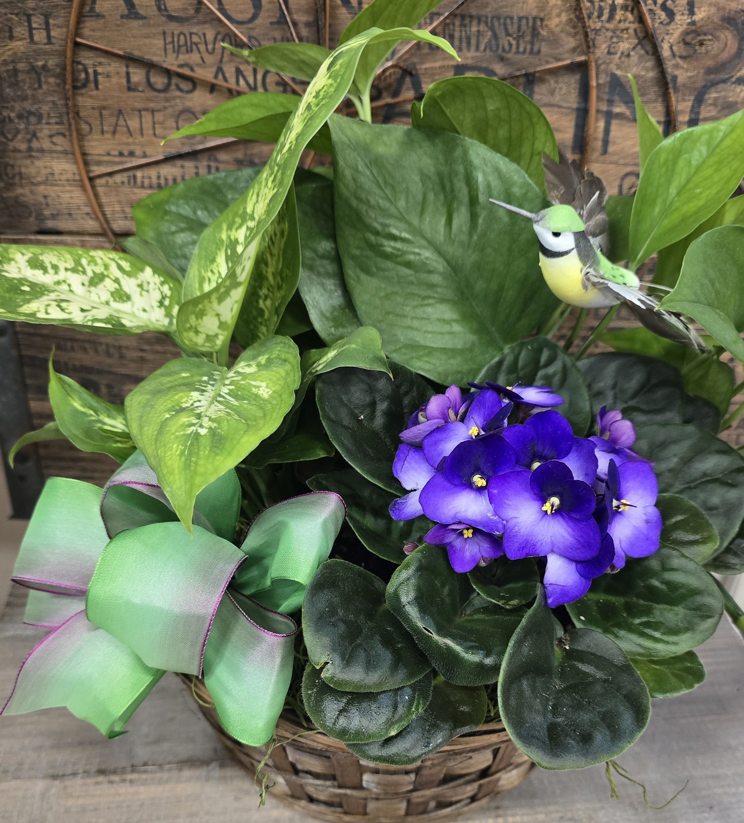 Potted plant arrangement with purple African violets and a decorative bird