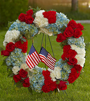 To Honor One's Country™ Wreath - Pay tribute to a life lived in devotion and service to country with a red, white and blue floral wreath embellished with the beloved stars and stripes. A fitting way to celebrate the life of a veteran, government worker or any American patriot, this beautiful, full ring of colorful flowers includes red roses, red and white carnations and blue hydrangeas, beautifully complemented by lush greens. It adds a tasteful salute of patriotism on a floor-standing easel at a wake, for funeral services and for graveside burial services. Approximately 28"H x 24"W. Your purchase includes a complimentary personalized gift message.
