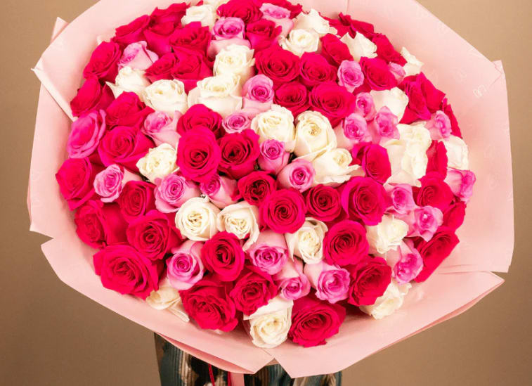Large bouquet of pink, red, and white roses wrapped in pale pink paper