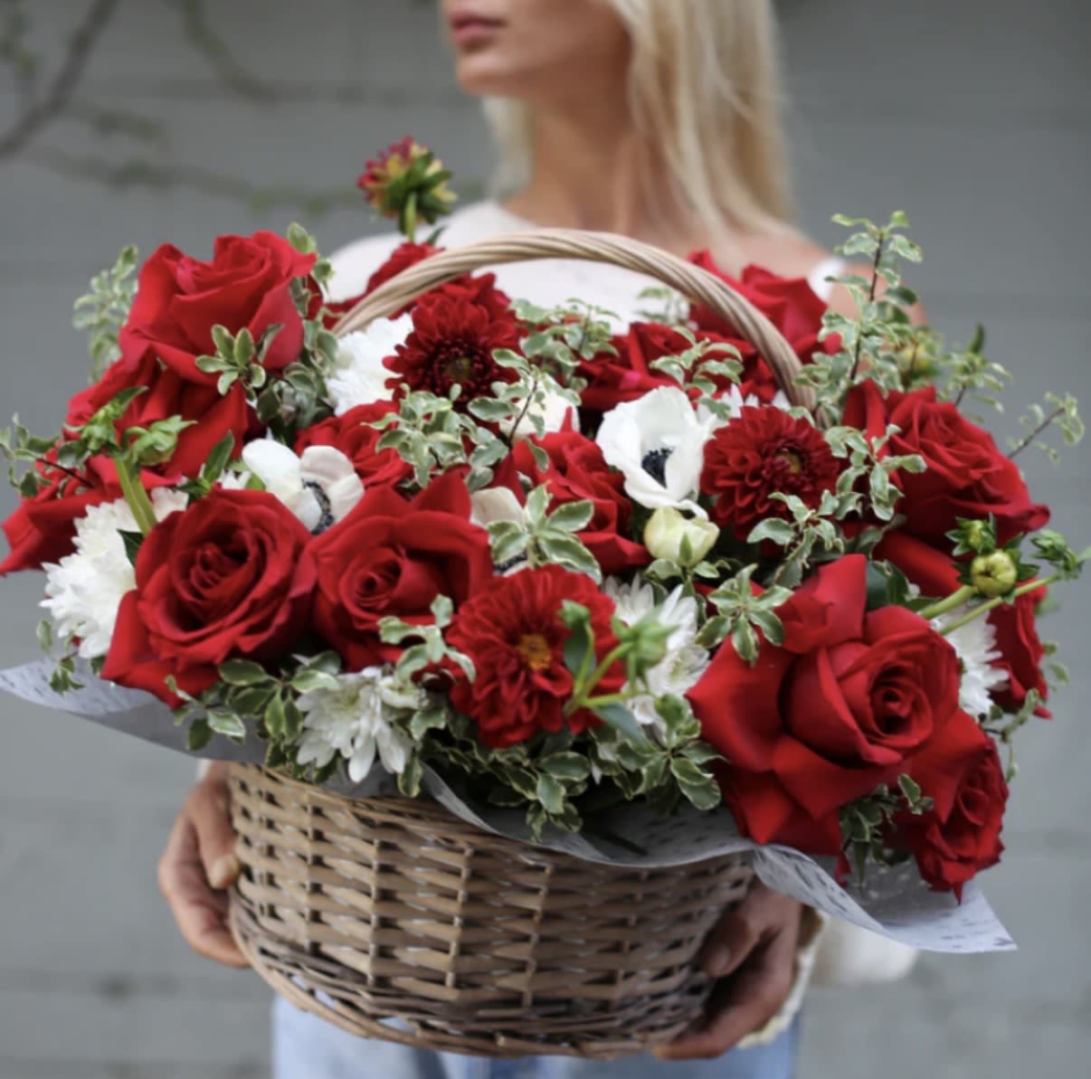 Basket of red roses and white flowers held by a woman