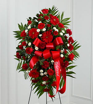 The FTD® Treasured Memories™ Standing Spray - The FTD® Treasured Memories™ Standing Spray is a rich and colorful way to express your unending love and devotion to the departed. An exceptional arrangement of red roses, burgundy carnations, burgundy mini carnations, red gerbera daisies and white button poms are accented with a variety of lush greens. A red ribbon with the word, "Beloved", embossed in a gold metallic lettering, finishes this beautiful display for their final farewell service. Displayed on a wire easel. Approximately 46"H x 30"W. Your purchase includes a complimentary personalized gift message.