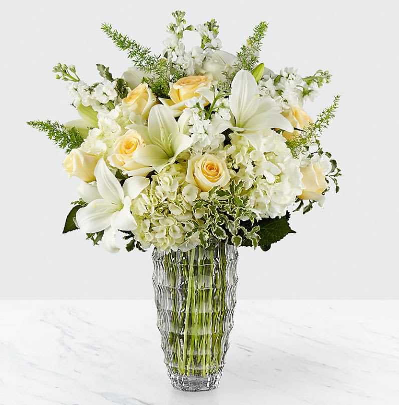 Hope Heals™ Luxury Bouquet - VASE INCLUDED - Offering a ray of light within what can be a dark place when grieving the loss of a loved one, The Hope Heals™ Luxury Bouquet is a unique and sophisticated way to show how much you care for your recipient and the memory of the deceased. An exquisite arrangement designed by our floral experts, this gorgeous bouquet brings together ivory roses, fragrant white gilly flowers, clouds of white hydrangea and star-shaped white Asiatic Lilies. Accented with asparagus fern fronds and variegated foliage, this sympathy bouquet is presented in a keepsake faceted clear glass vase to create an exceptional look that is not only a tribute to a life well lived, but a comfort to those left behind. IMPRESSIVE bouquet is approx. 23"H x 19"W. STUNNING bouquet is approx. 25"H x 21"W.