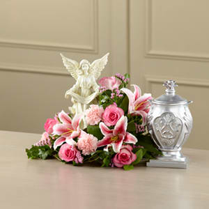 Pink floral arrangement with lilies and roses beside a silver urn and angel figurine
