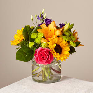 Bouquet of sunflowers, roses, and purple blooms in a glass vase