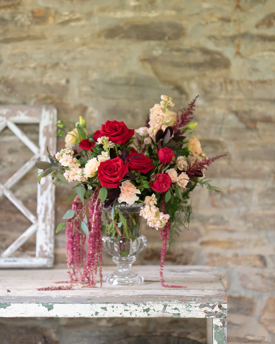 Red roses and blush flowers arranged in a clear glass vase