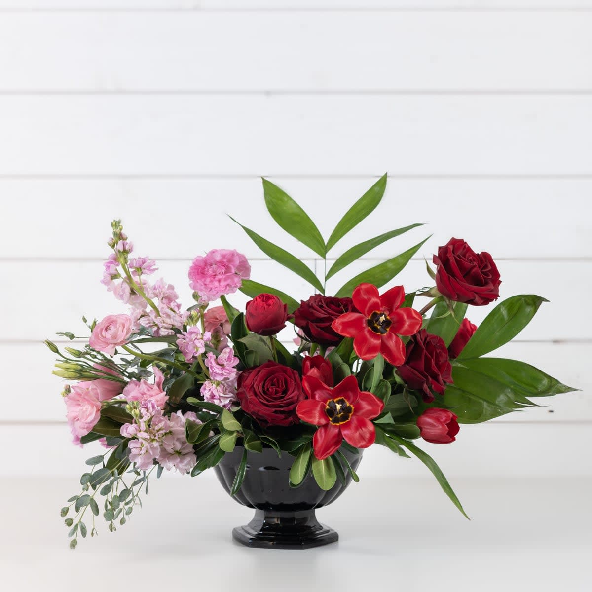 Red and pink floral arrangement in a black pedestal vase