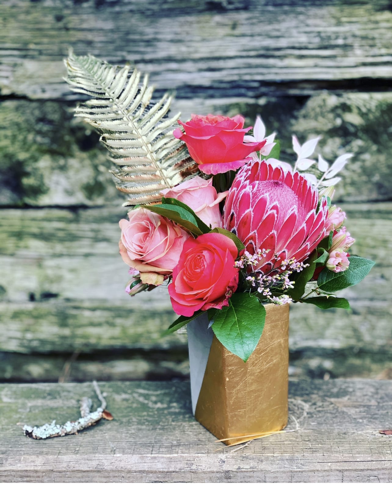 Pink roses and a protea in a gold vase