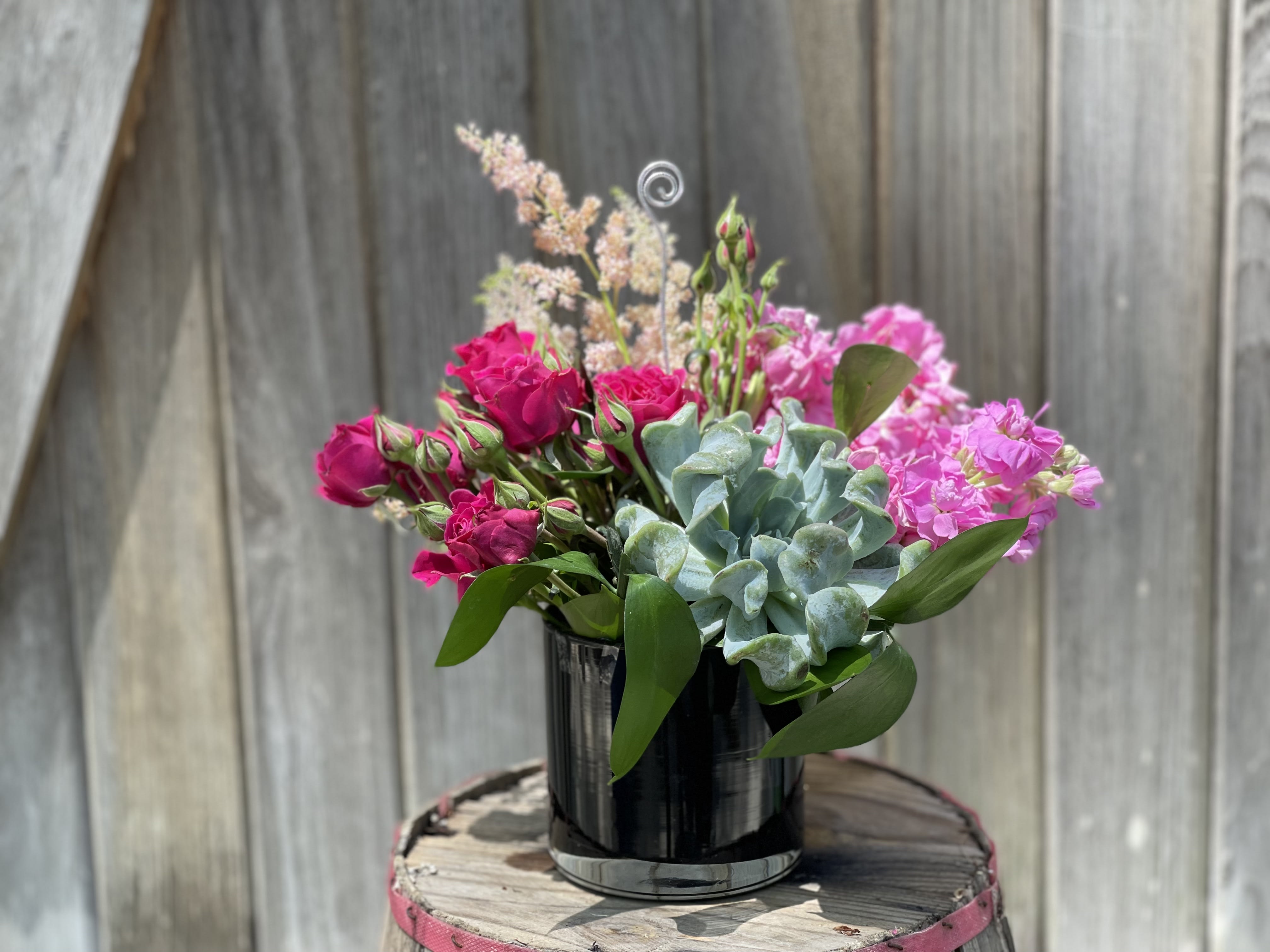 Pink roses and carnations arranged with a succulent in a black vase