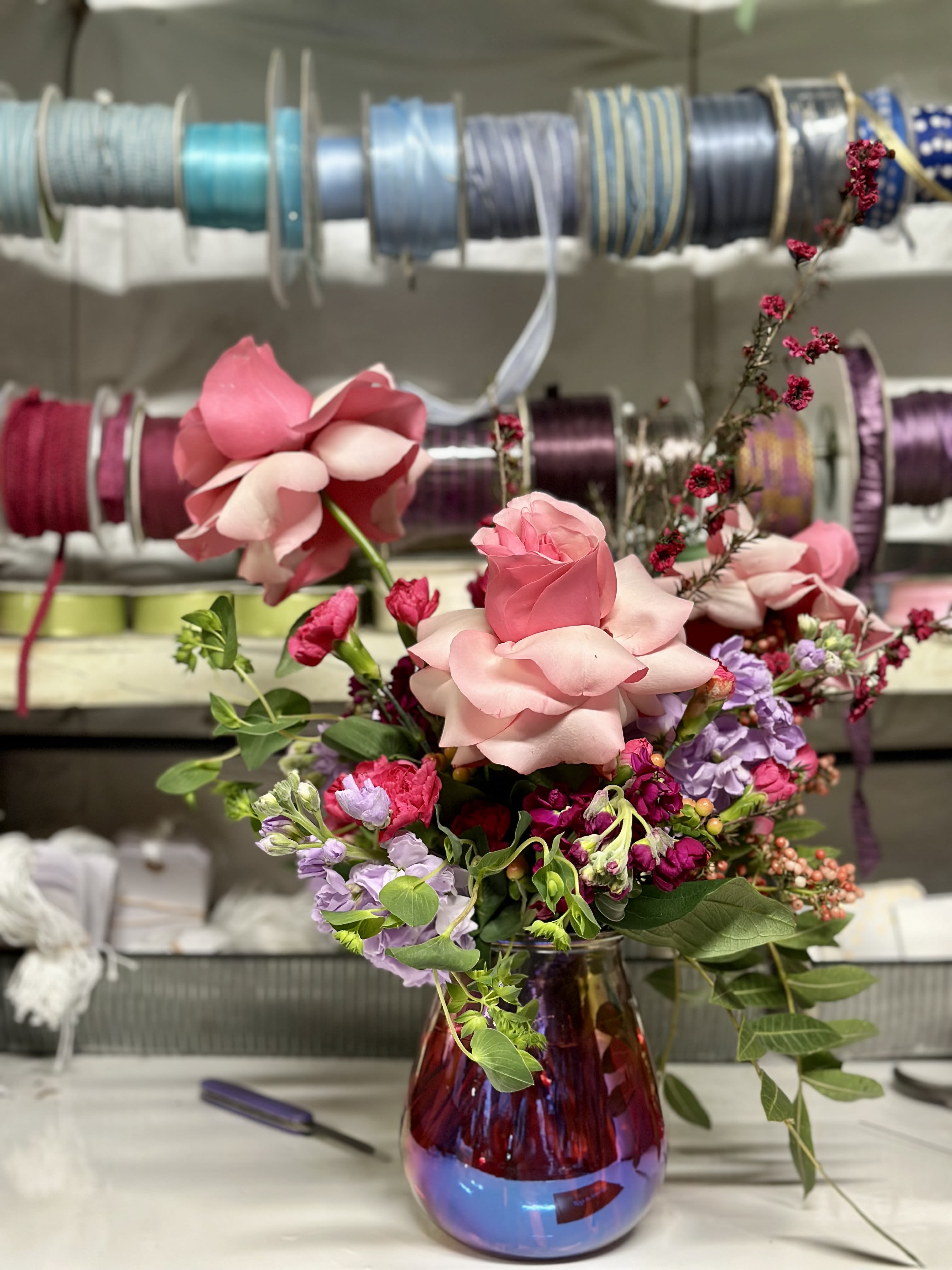Pink rose bouquet in a purple glass vase with lavender flowers