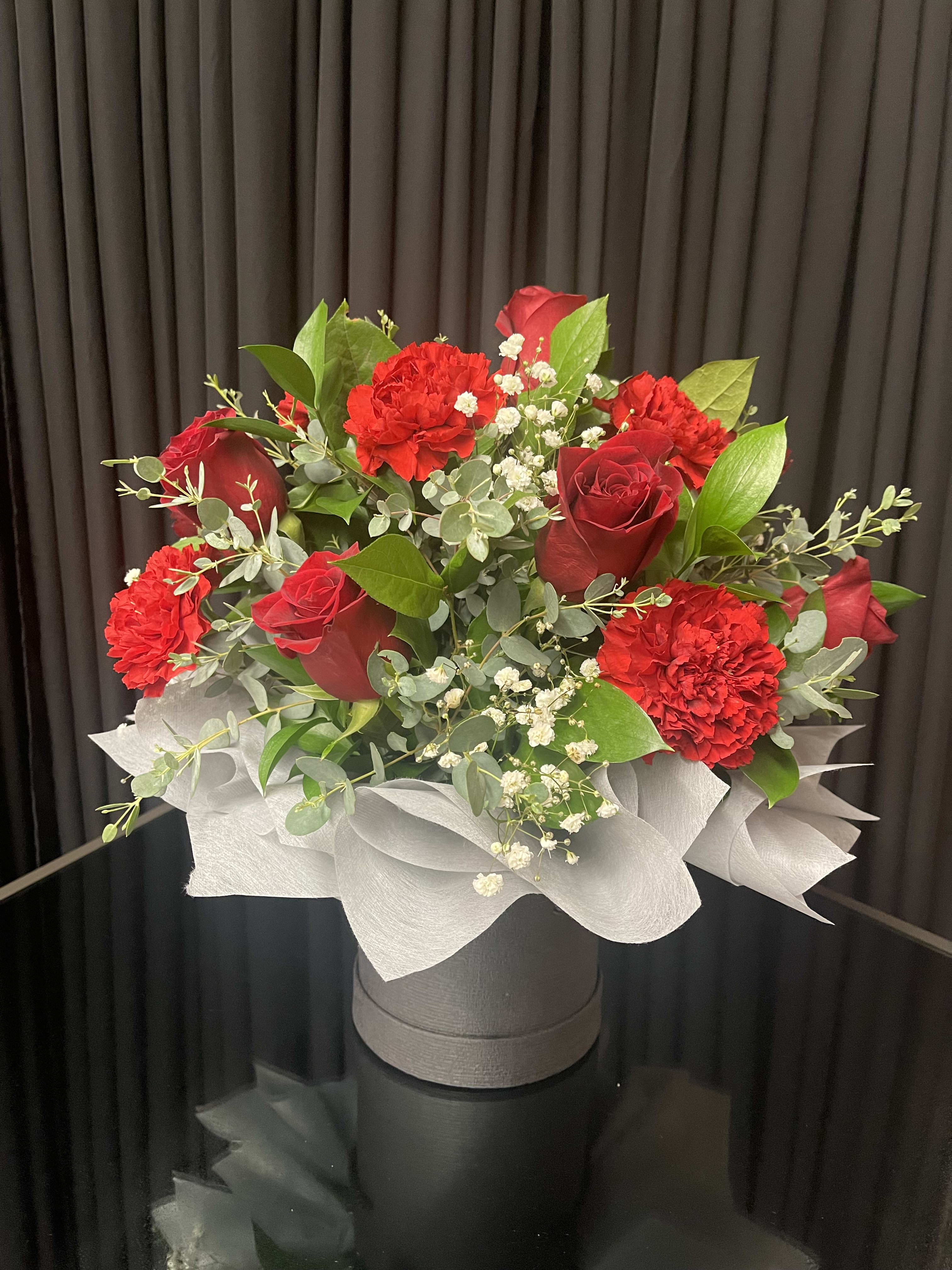 Red Celebration Explosion - Explosion arrangement is build on a top hat cylinder filled with oasis holding this beautiful piece together. Arranged with beautiful red roses, red carnations, Gypsophila, salal Leaves, and Eucalyptus branches. 
