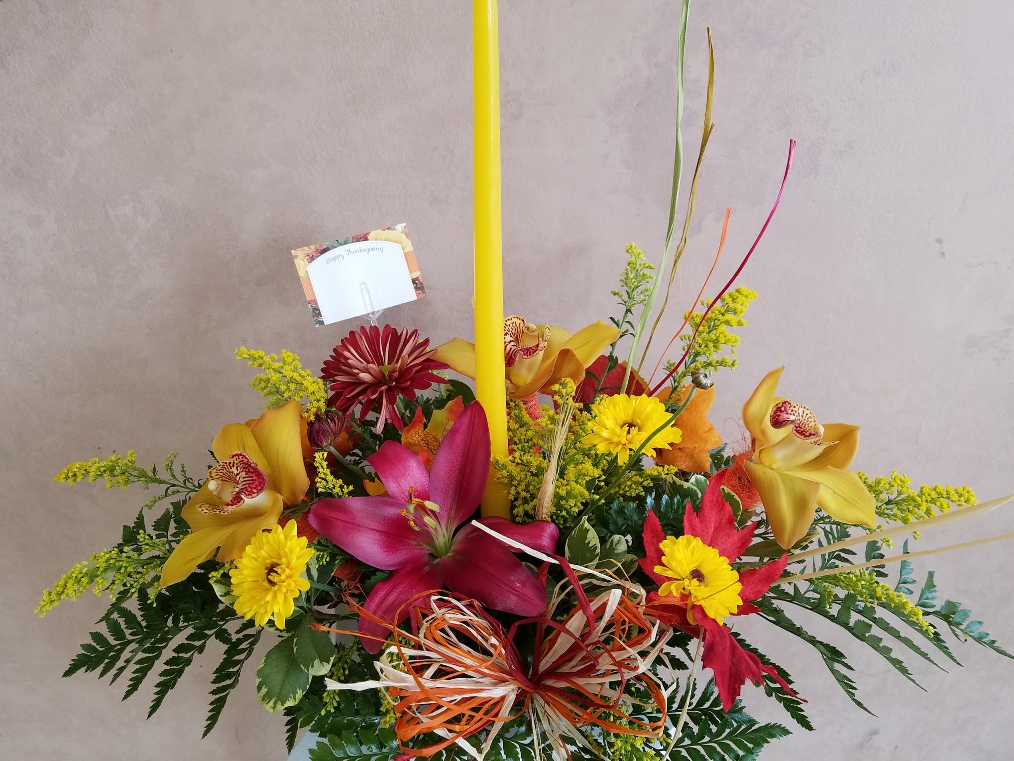 TG 1 - Thanksgiving centerpiece featuring an assortment of fall flowers arranged in a floral foam container.  * Candle color and florals may vary based on availability.