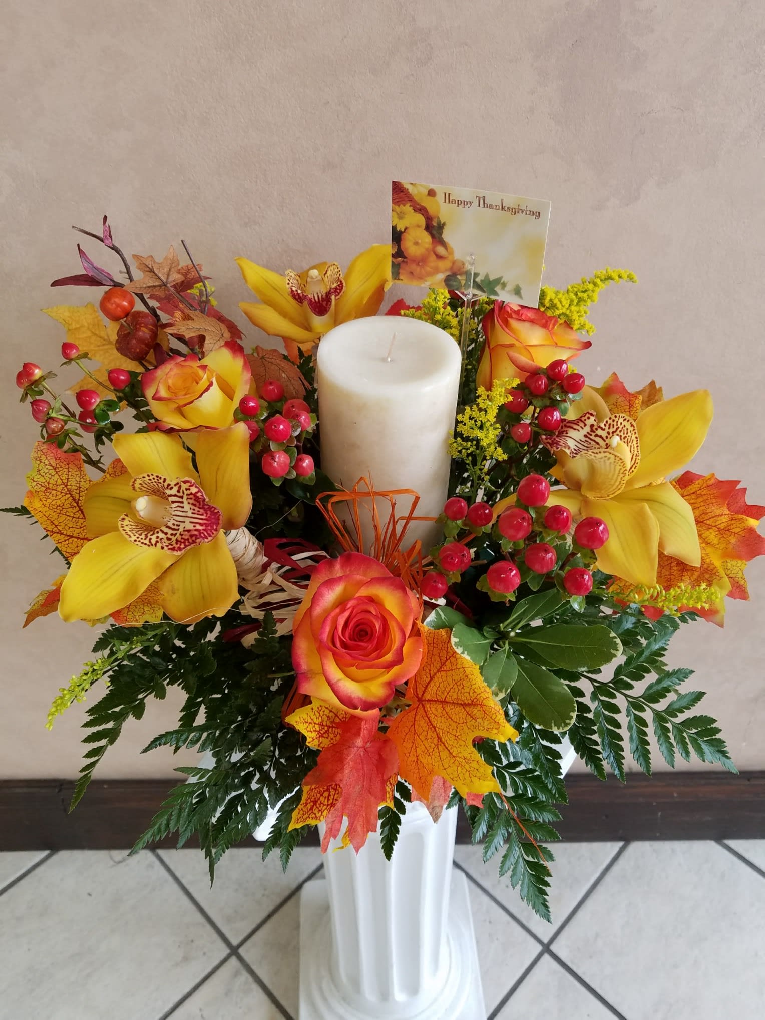 Yellow orchids and roses arranged around a white pillar candle in a vase