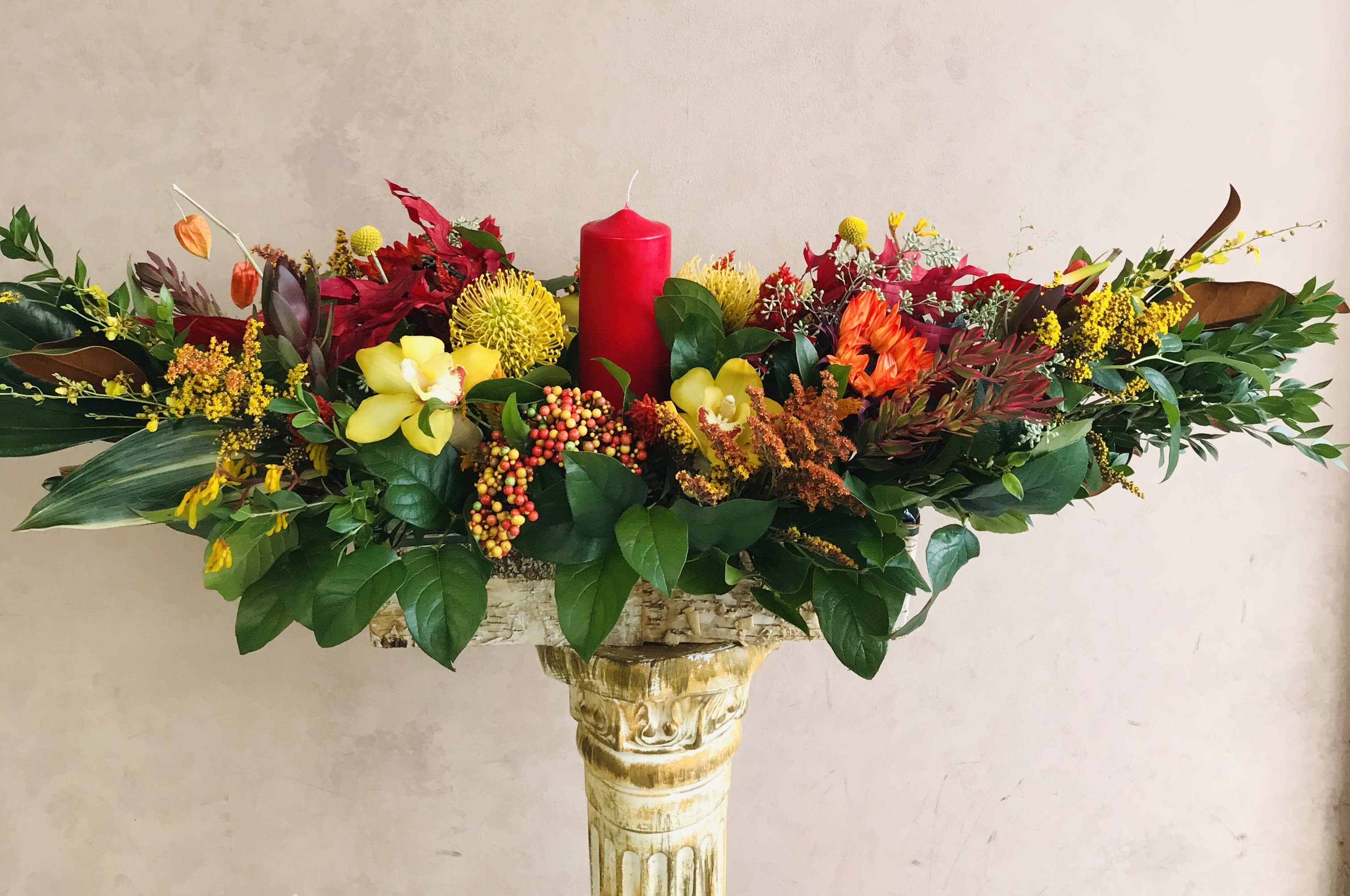 TG3 - Thanksgiving centerpiece featuring an assortment of fall flowers arranged in a floral foam container.  * Candle color and florals may vary based on availability.