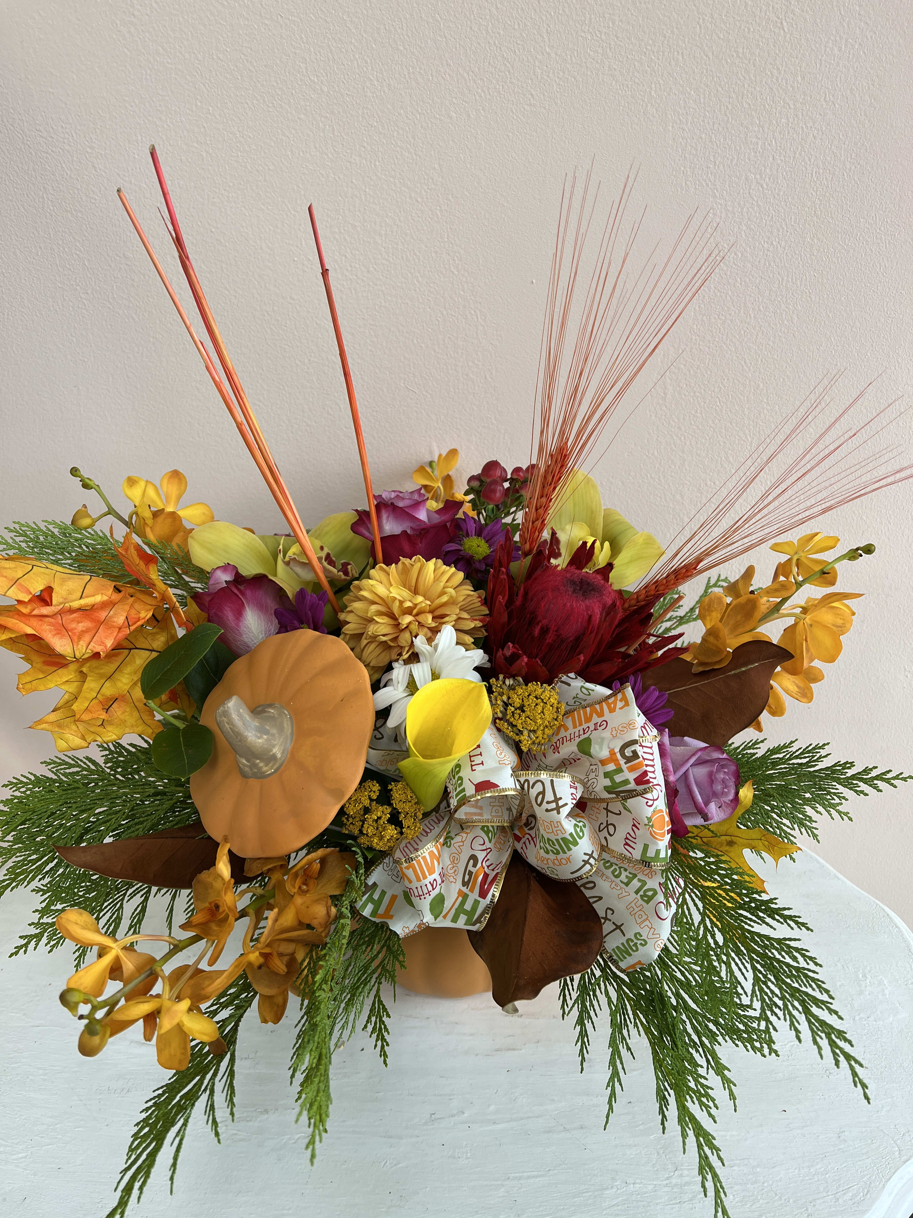 TG 9 - Thanksgiving centerpiece featuring an assortment of fall flowers arranged in a floral foam container.  * Candle color and florals may vary based on availability.