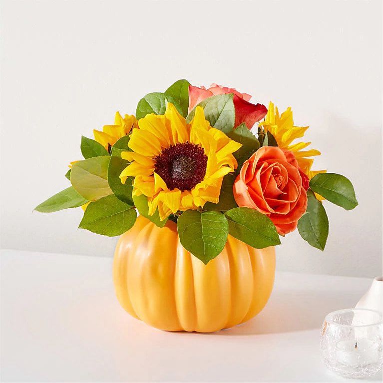 Autumn Pumpkin - A bright and colorful centerpiece arranged in a ceramic pumpkin container. This arrangement features roses, sunflowers, and greenery.