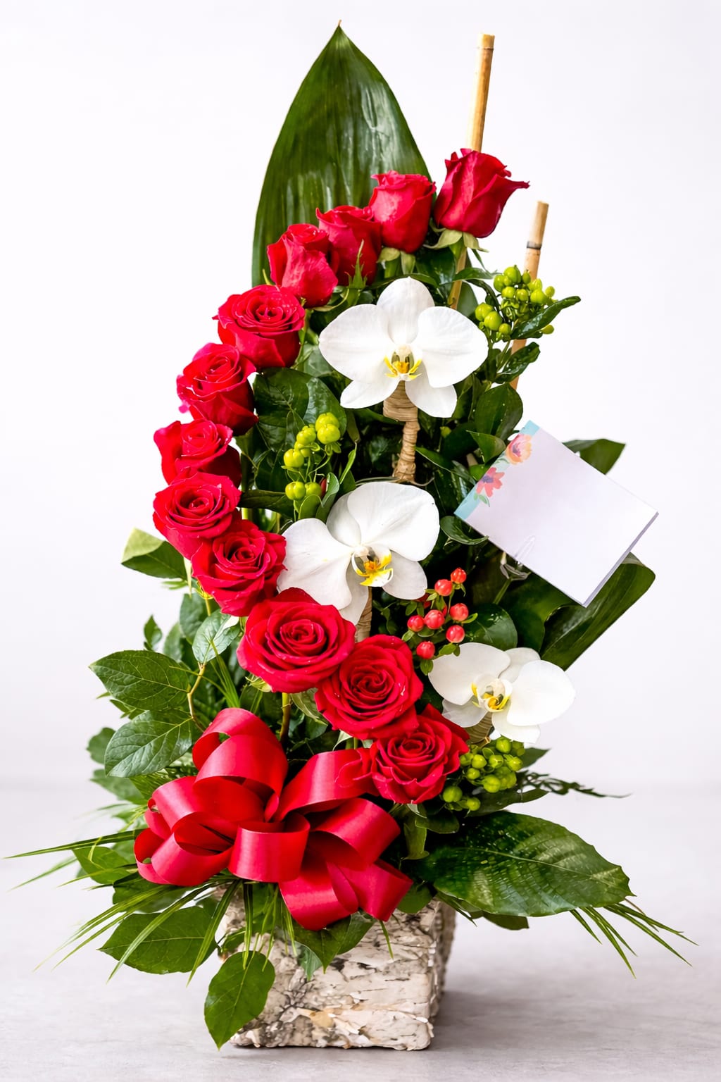 Red roses and white orchids in a square vase with a red ribbon