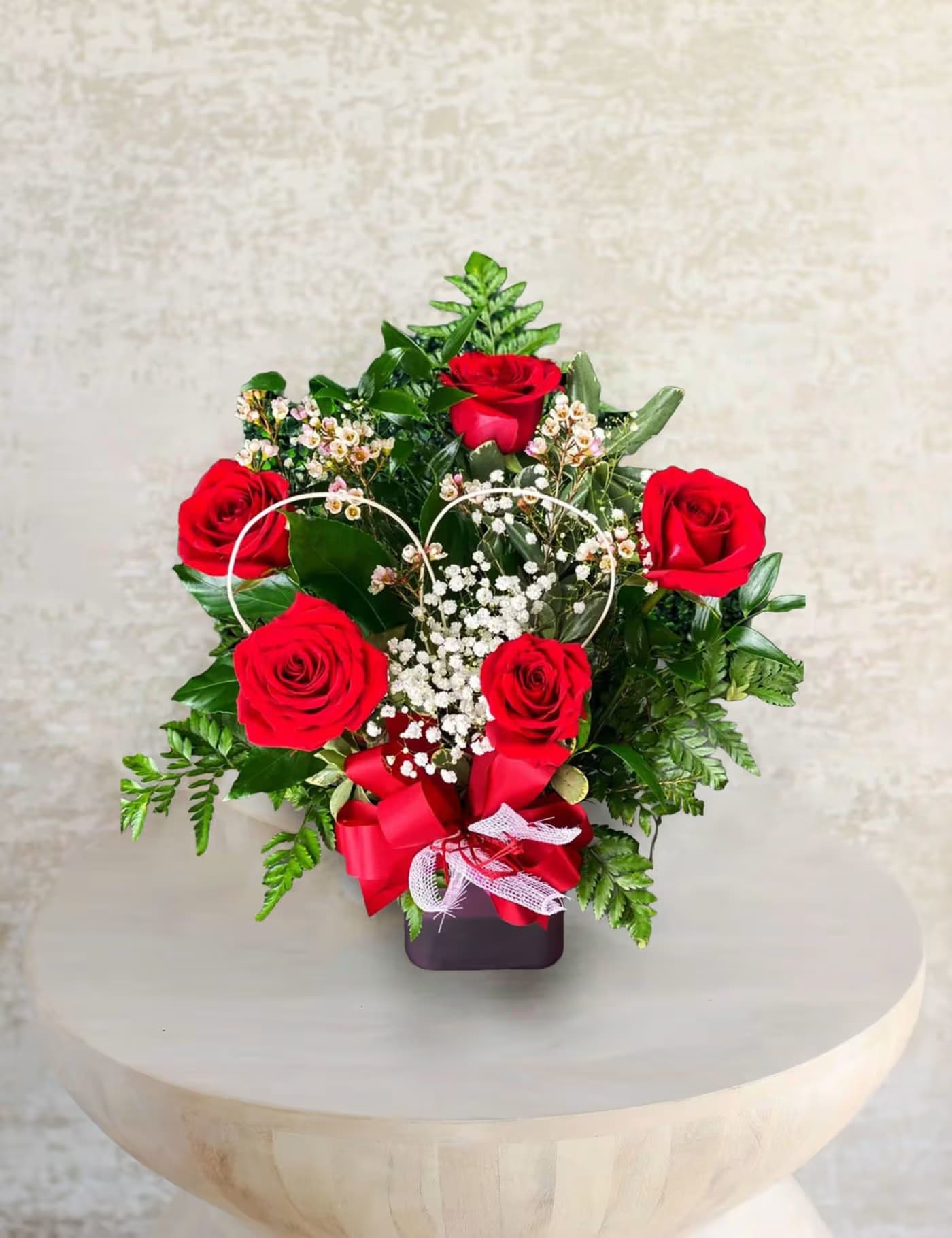 Red roses arranged in a heart-shaped design with baby's breath in a dark vase
