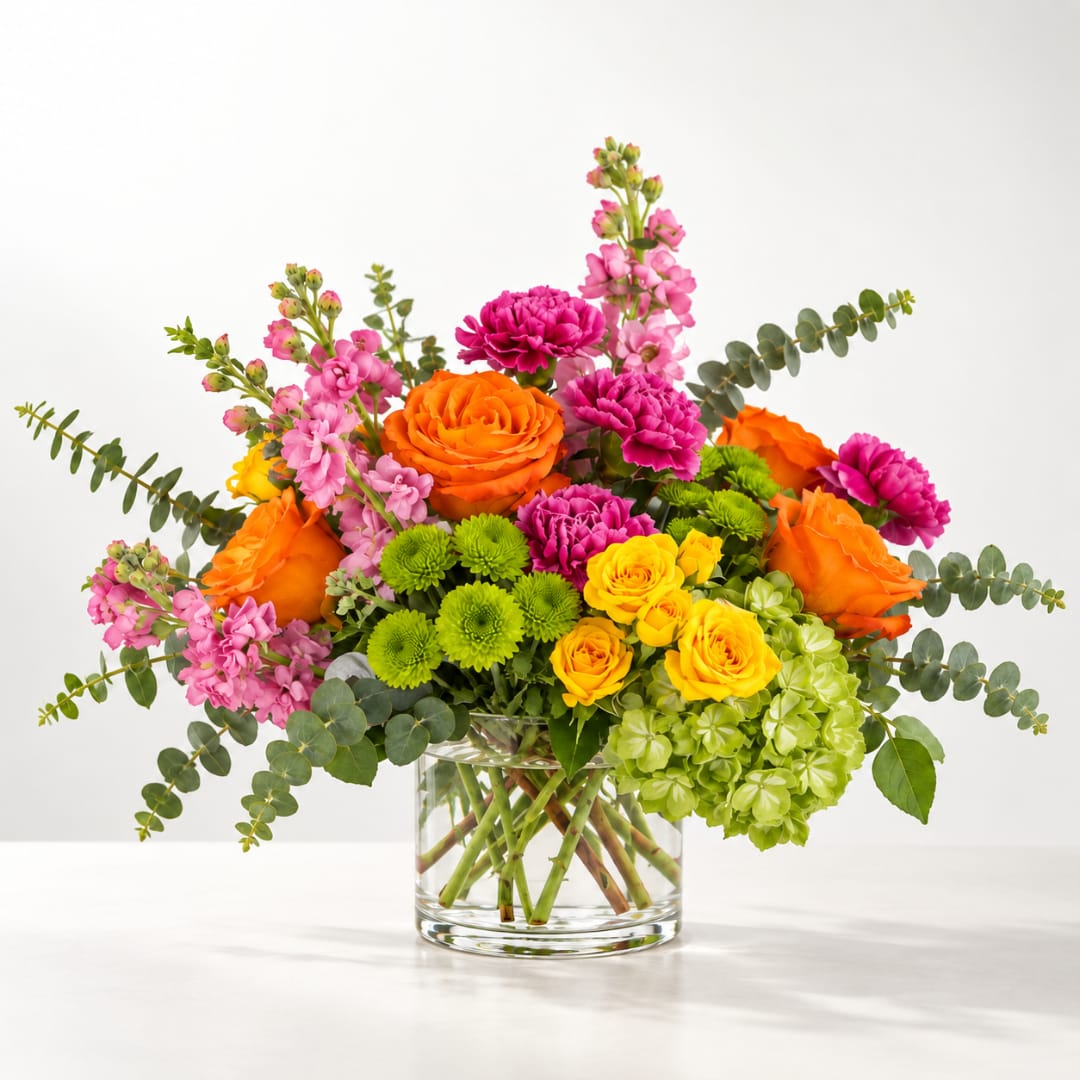 Bright mixed bouquet in a clear glass vase with orange, pink, yellow, and green blooms