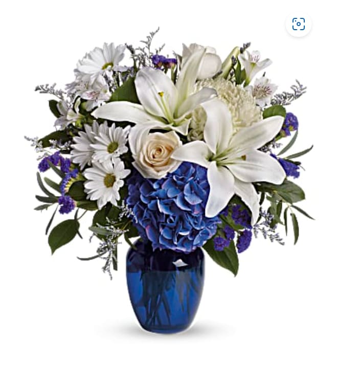 Beautiful in Blue ( TeleFlora ) - Blooms such as blue hydrangea, crème roses, graceful white oriental lilies, white alstroemeria, a white disbud mum, purple statice and lavender limonium are accented by seeded eucalyptus and salal in a stunning cobalt blue glass vase.