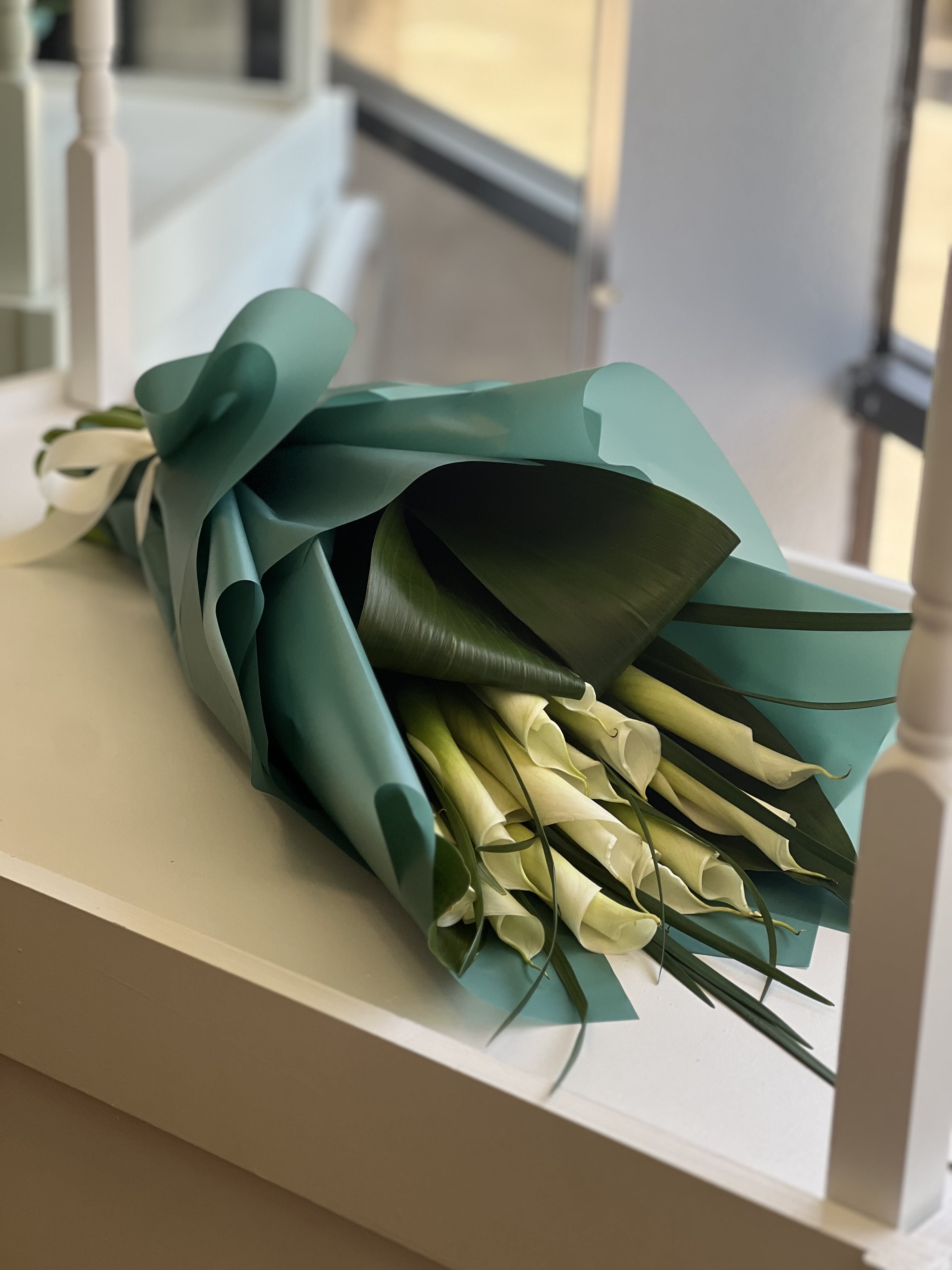 Bouquet of white calla lilies wrapped in teal paper
