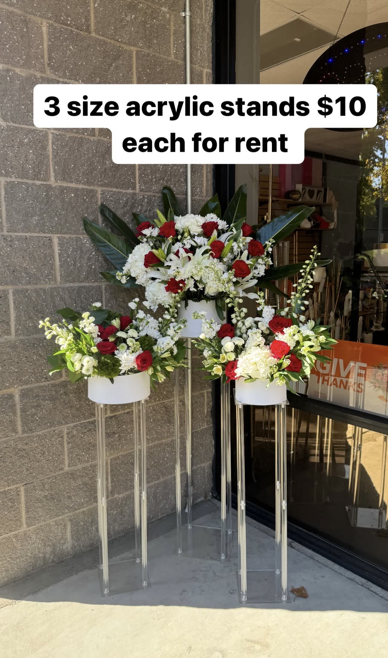 Three floral arrangements on clear acrylic stands with red and white flowers