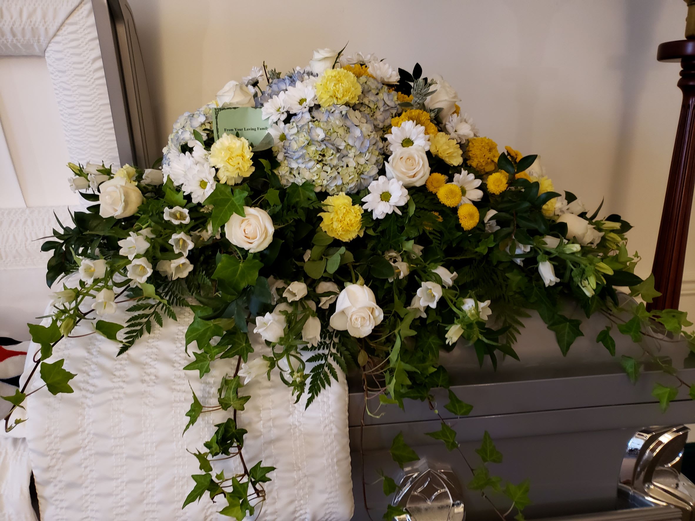 Large white and yellow funeral spray with roses, daisies, and hydrangea