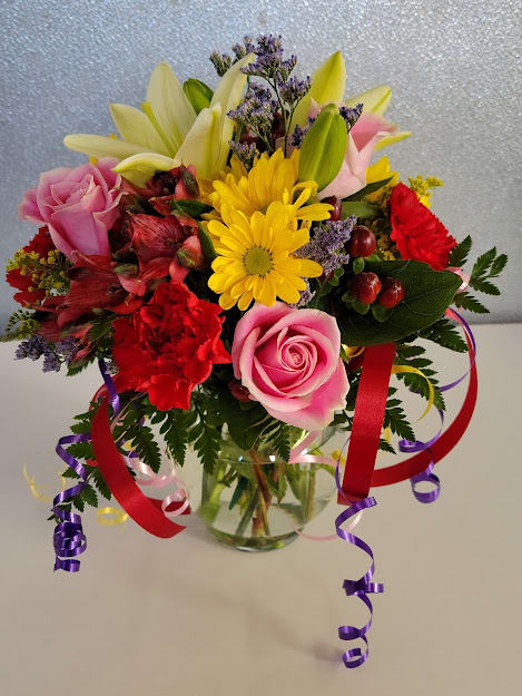 Mixed bouquet of pink roses, lilies, and yellow daisies in a glass vase