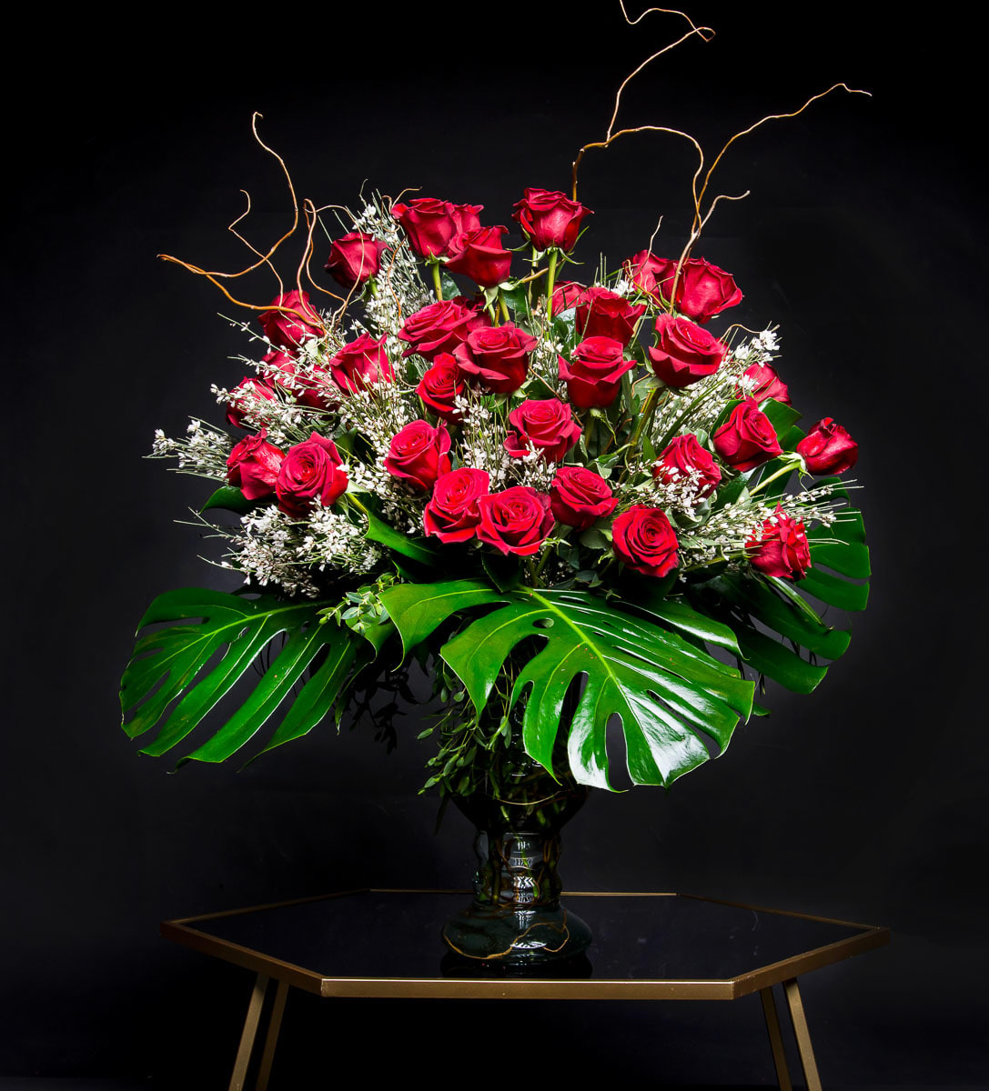 Large bouquet of red roses in a glass vase with tropical leaves