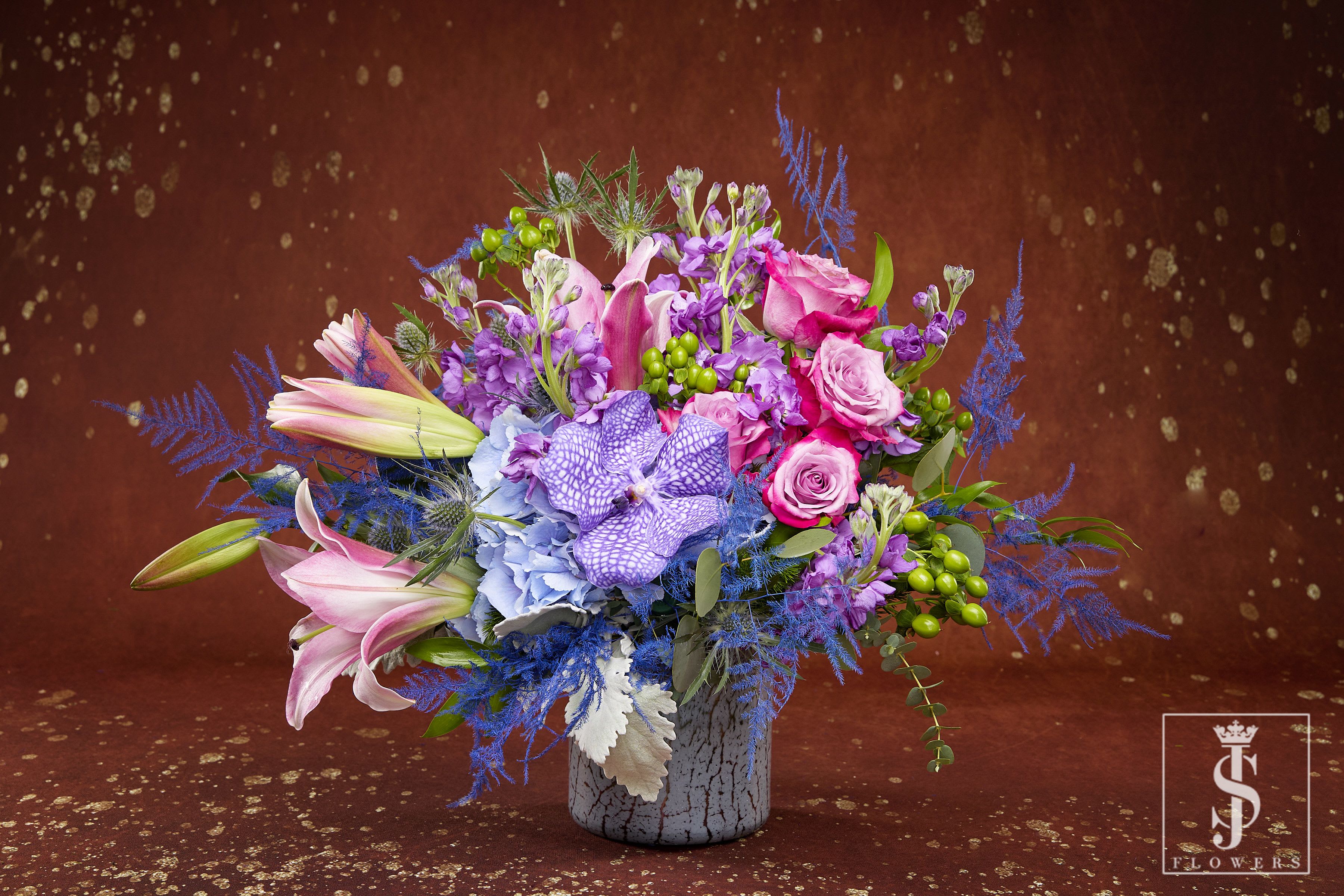 Colorful bouquet of lilies, roses, and orchids in a gray vase