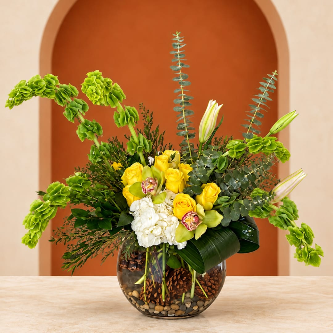 Yellow roses and white orchids in a glass bowl vase with greenery