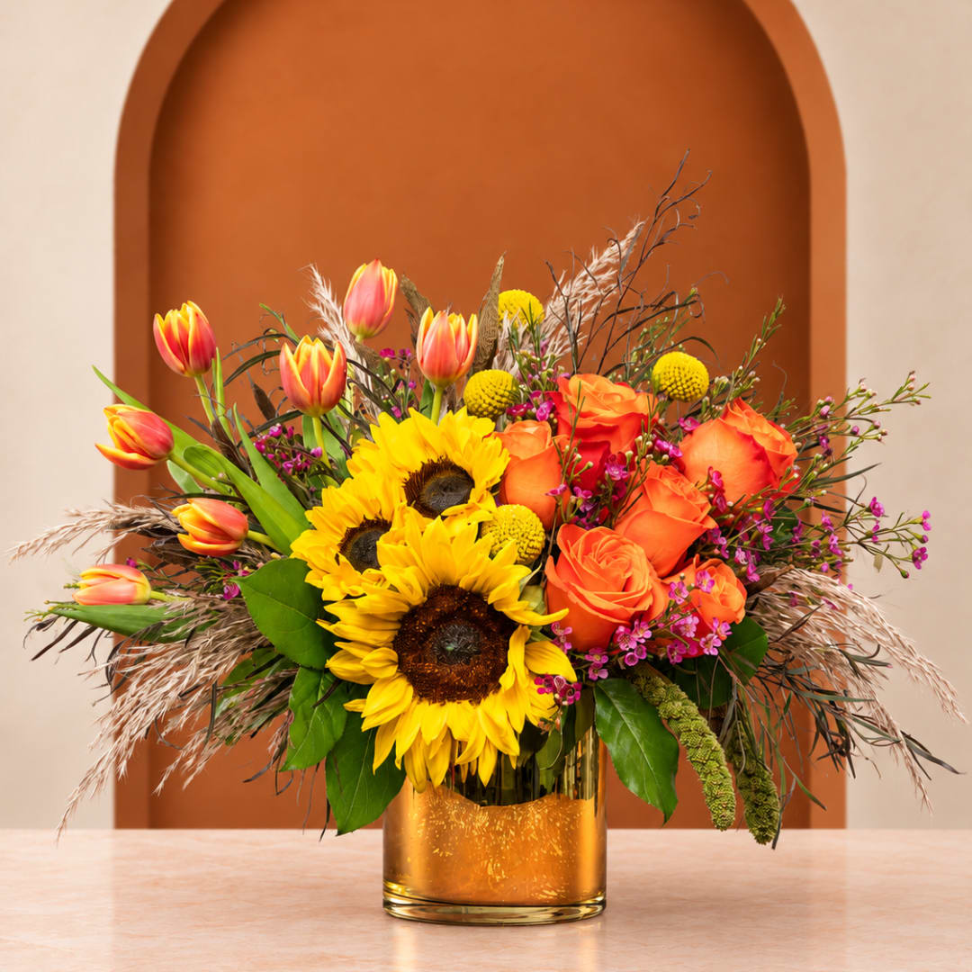 Sunflowers, orange roses, and tulips in a gold vase