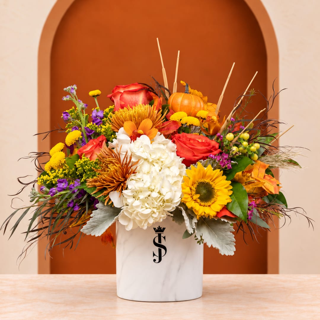Autumn floral arrangement in a white vase with roses, sunflowers, and a pumpkin accent.
