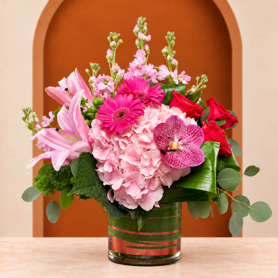 Pink and red floral arrangement in a glass vase with lilies and orchids