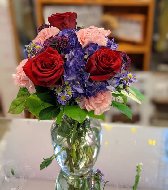 Bouquet of red roses, pink carnations, and blue hydrangeas in a glass vase