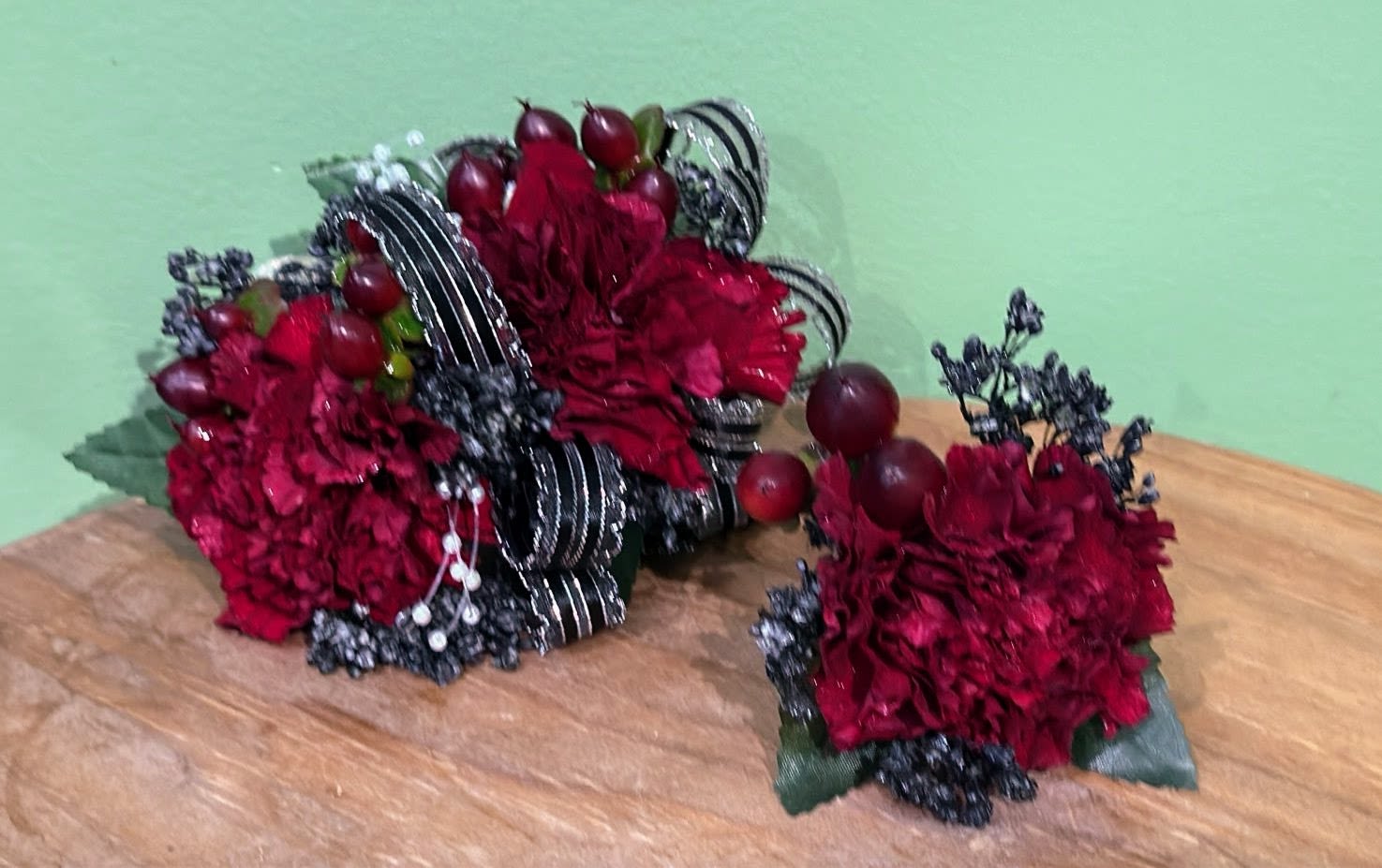 Two red floral arrangements with dark ribbon and berry accents on a table