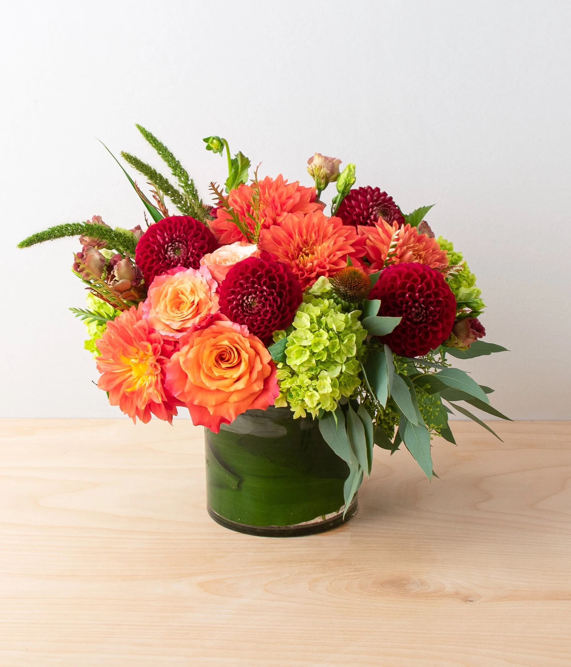 Orange and red mixed flower arrangement in a green glass vase