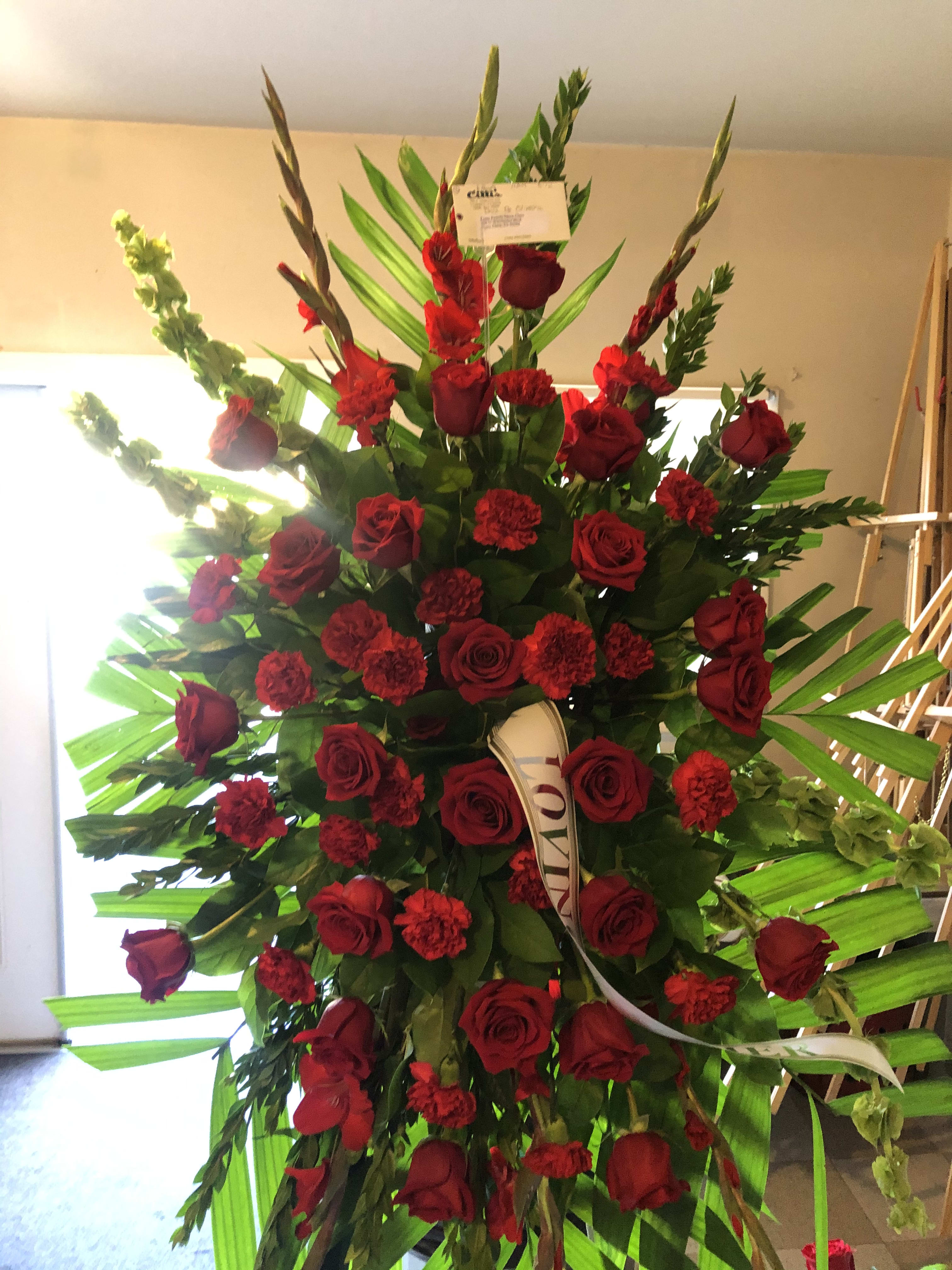 Tall standing arrangement of red roses and carnations with palm leaves