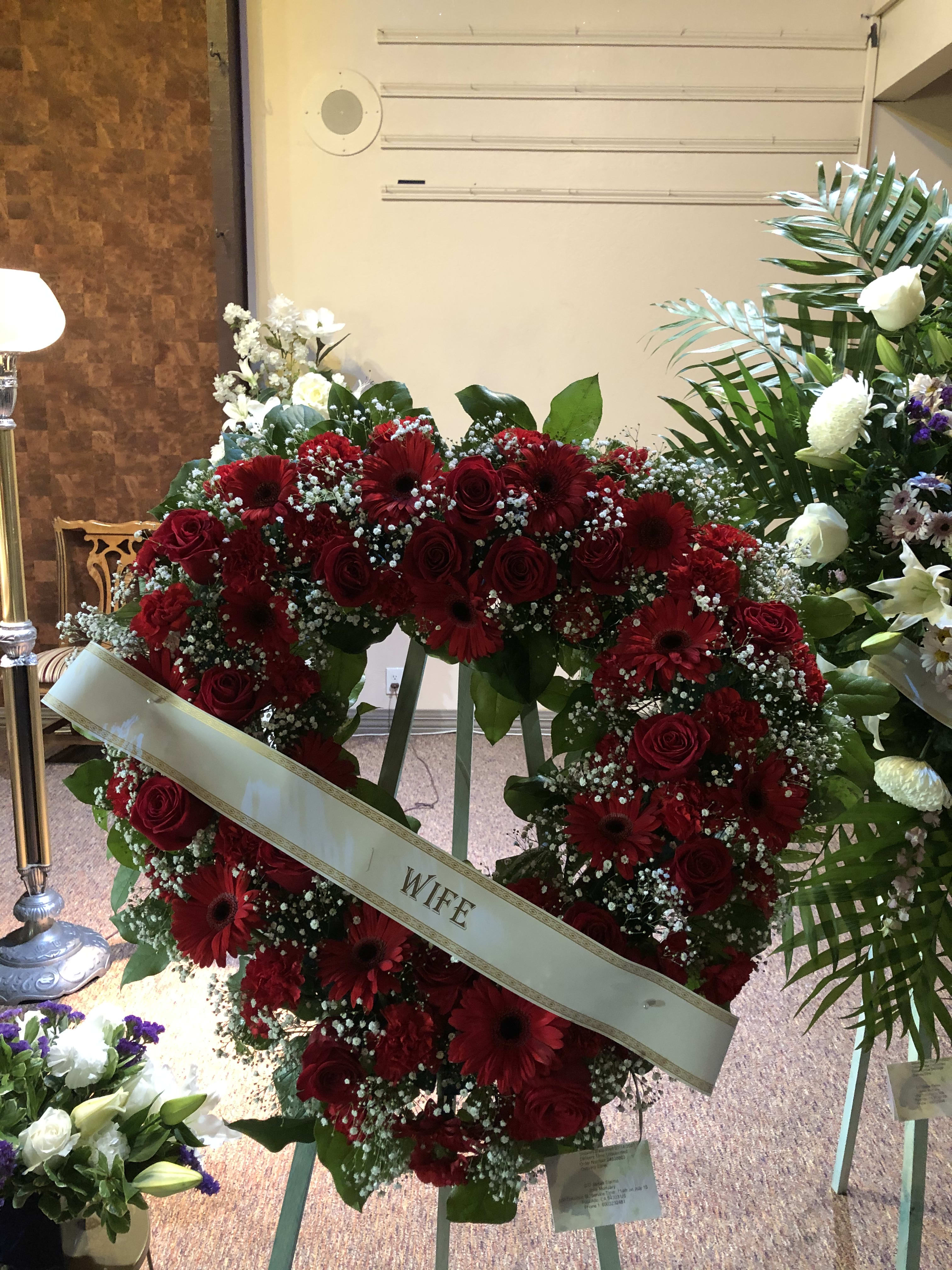 Heart-shaped red rose and gerbera wreath with a "WIFE" ribbon