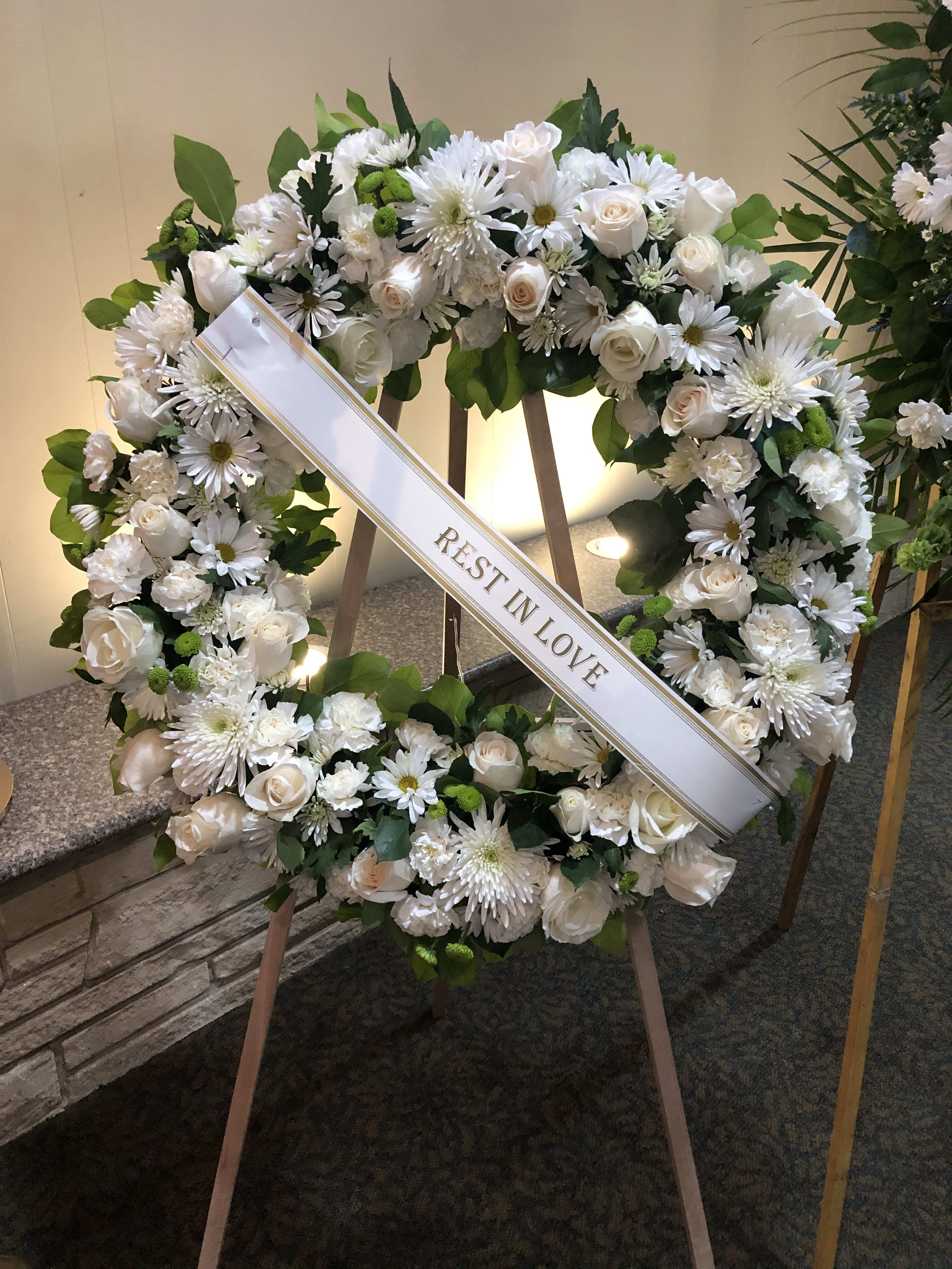 White floral funeral wreath with a "Rest in Love" ribbon