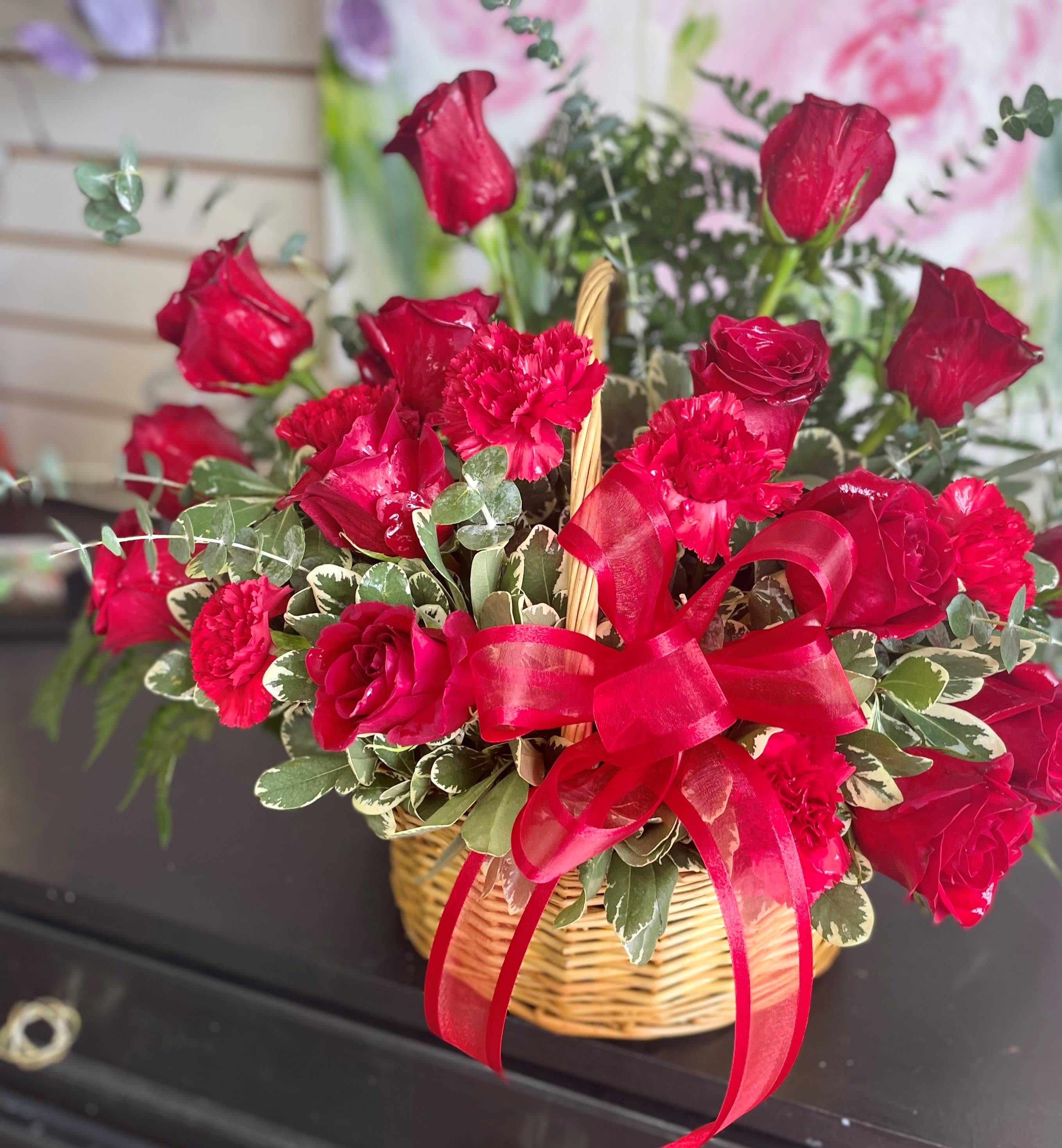 Red roses and carnations in a wicker basket with a red ribbon