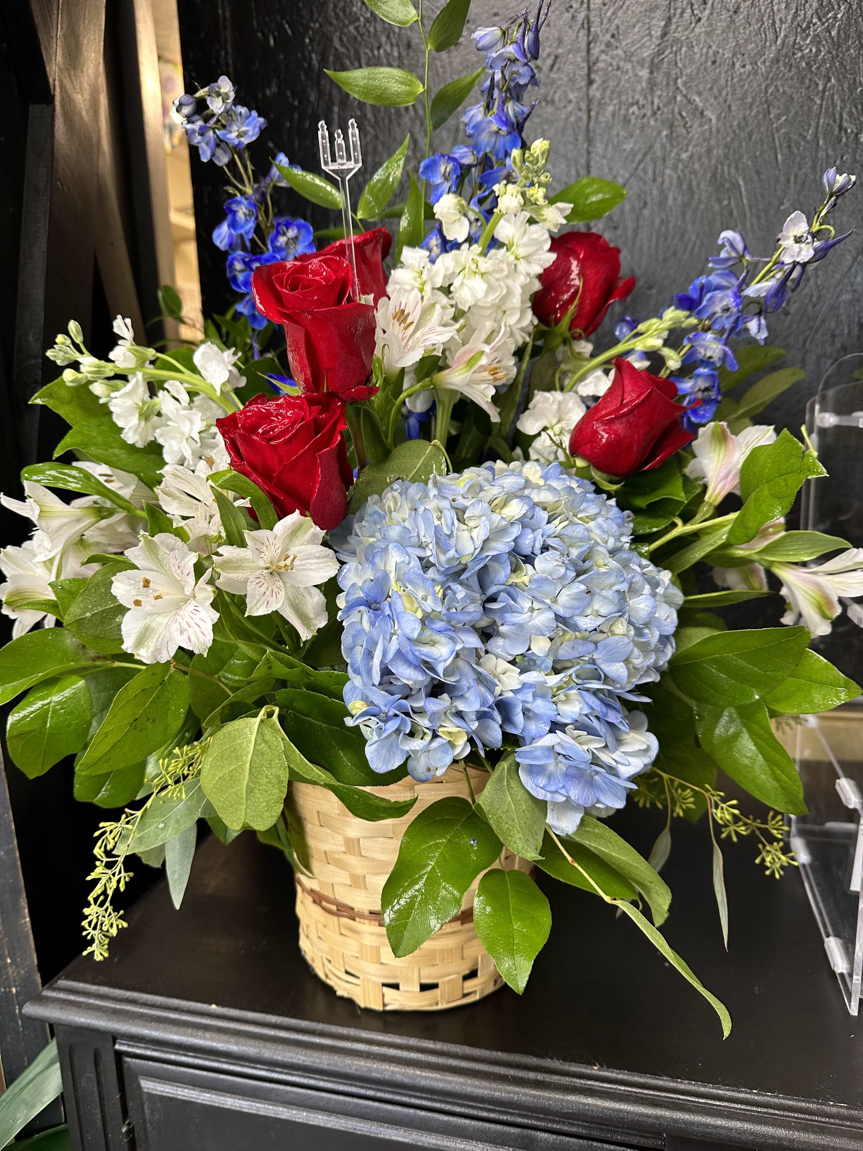 Forever Remembered  - A red, white, and blue tribute funeral basket featuring red roses, , blue delphinium, and white stock. Fitting for any type of funeral ceremony.