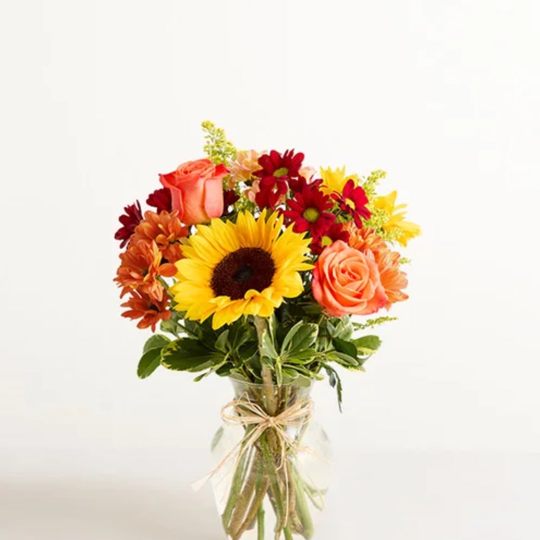 Bouquet of sunflowers, roses, and daisies in a glass vase