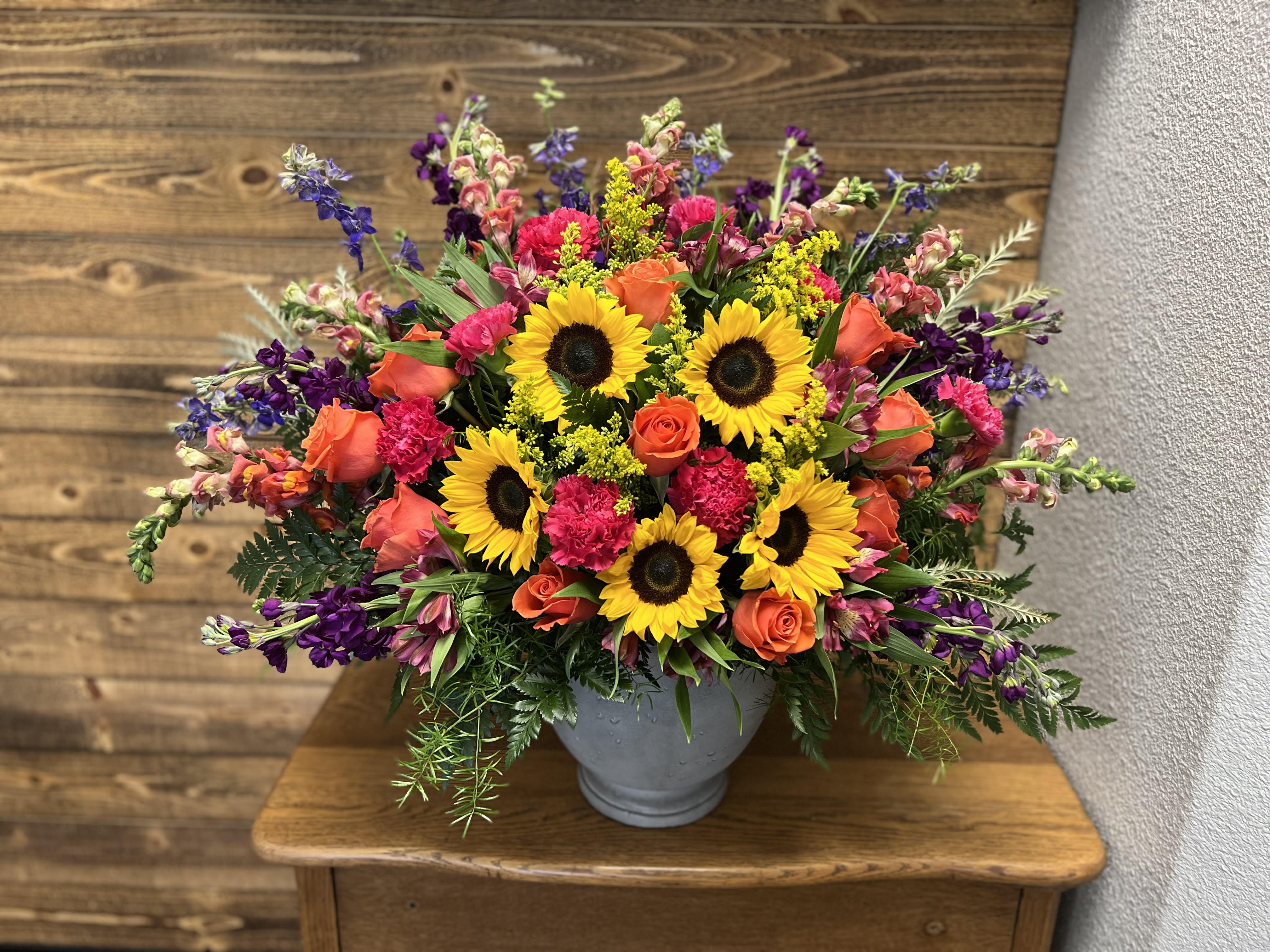 Mixed bouquet with sunflowers, orange roses, and purple flowers in a gray vase