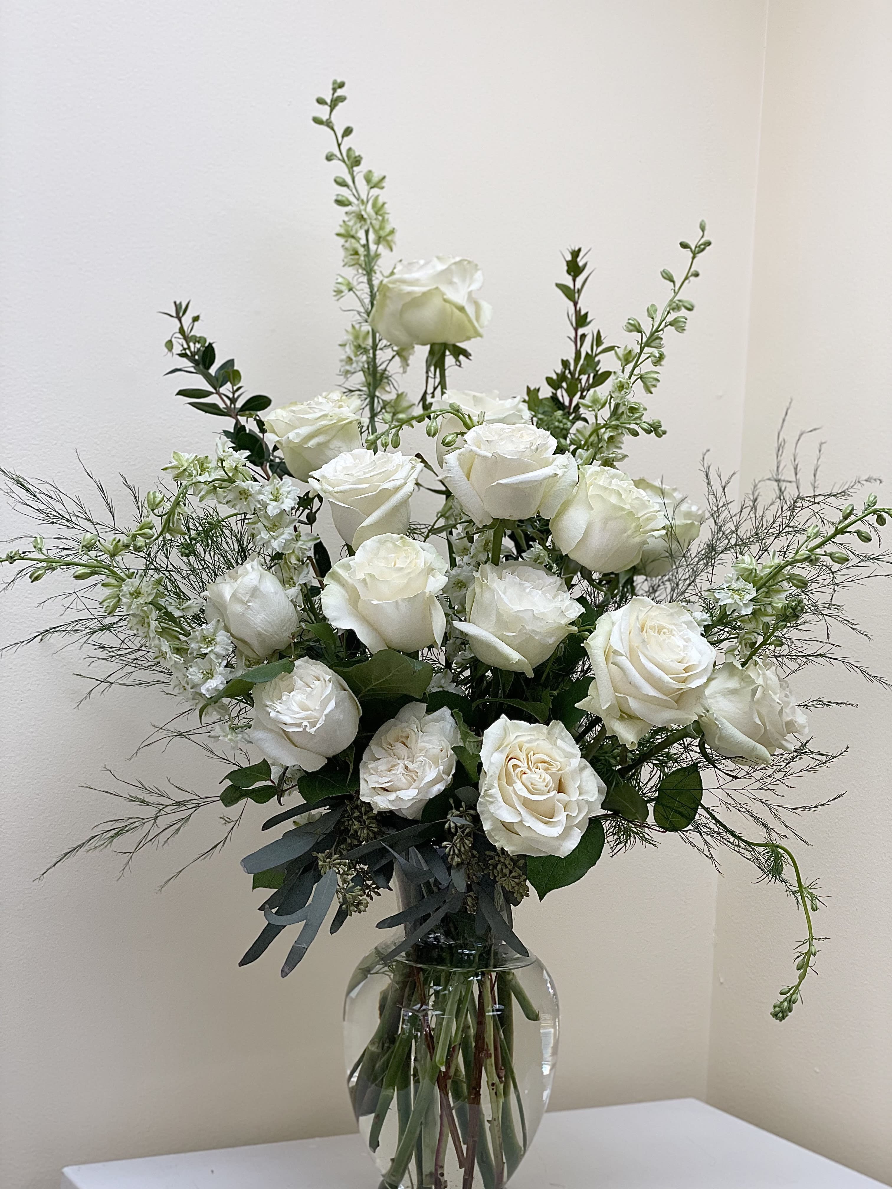 White roses arranged in a clear glass vase with airy greenery
