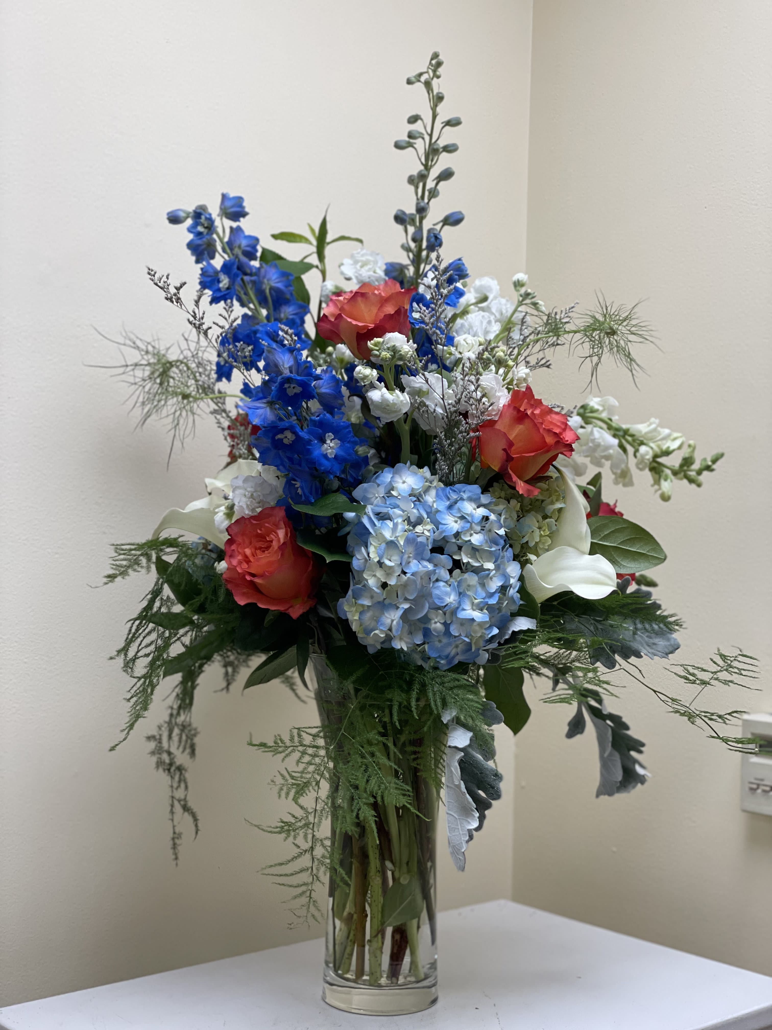Tall mixed bouquet with blue hydrangeas, red roses, and white calla lilies in a glass vase